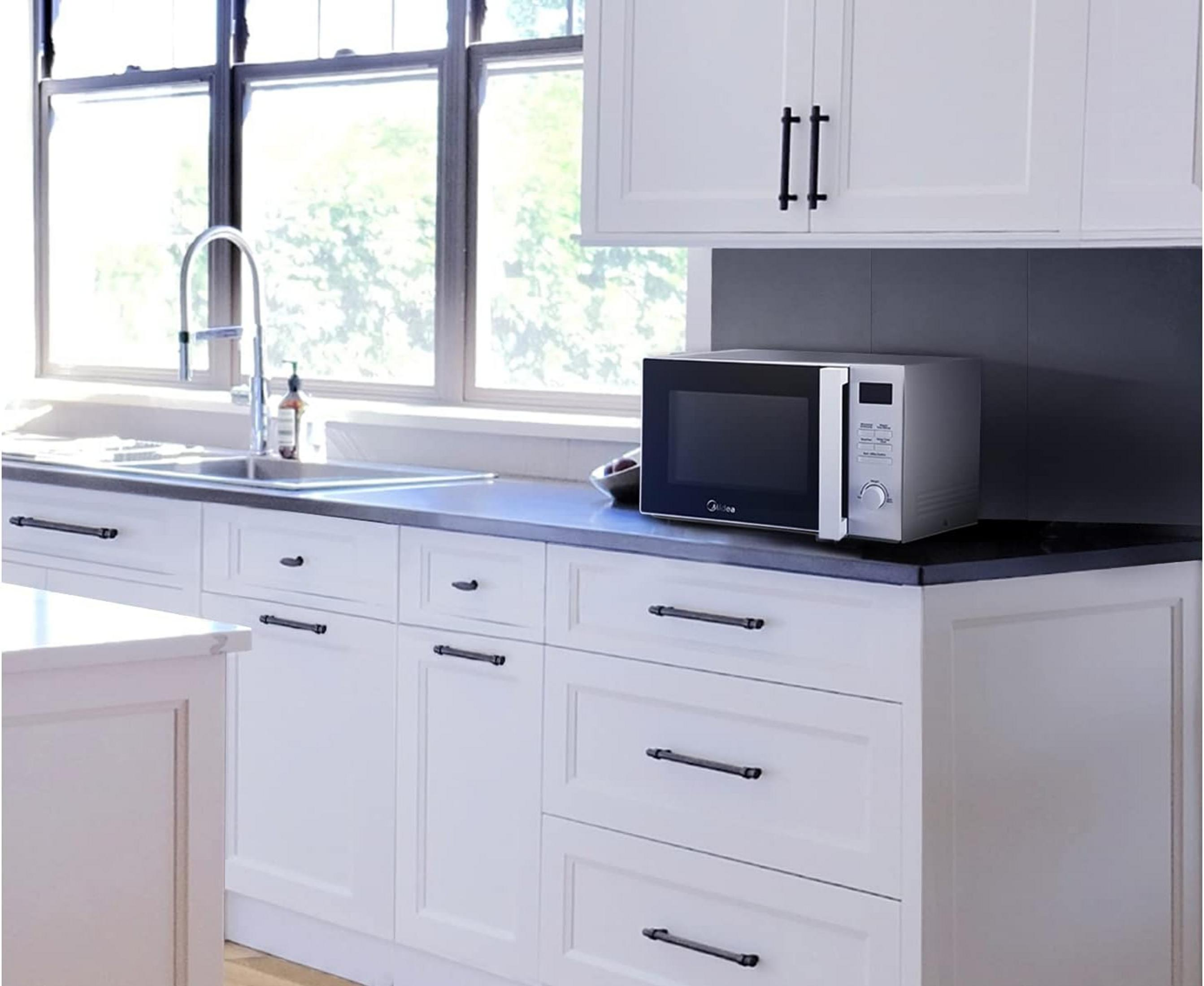 Una cocina blanca con un microondas plateado en la encimera.