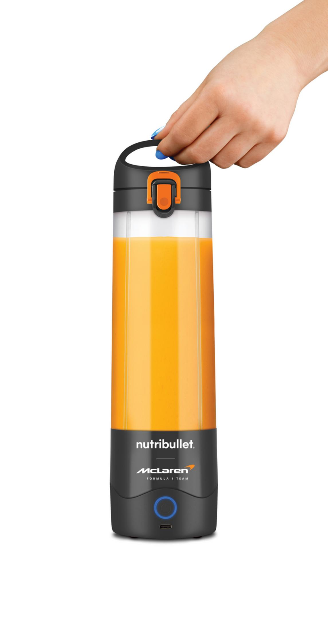 Una mano tiene una tazza Nutribullet con succo d'arancia, logo McLaren.