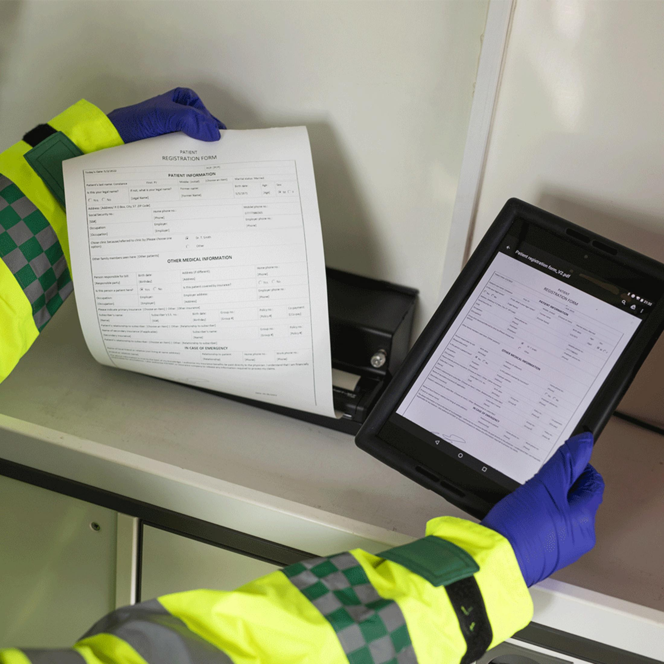 Person in Warnweste mit blauen Handschuhen hält ein Patientenformular und ein Tablet.