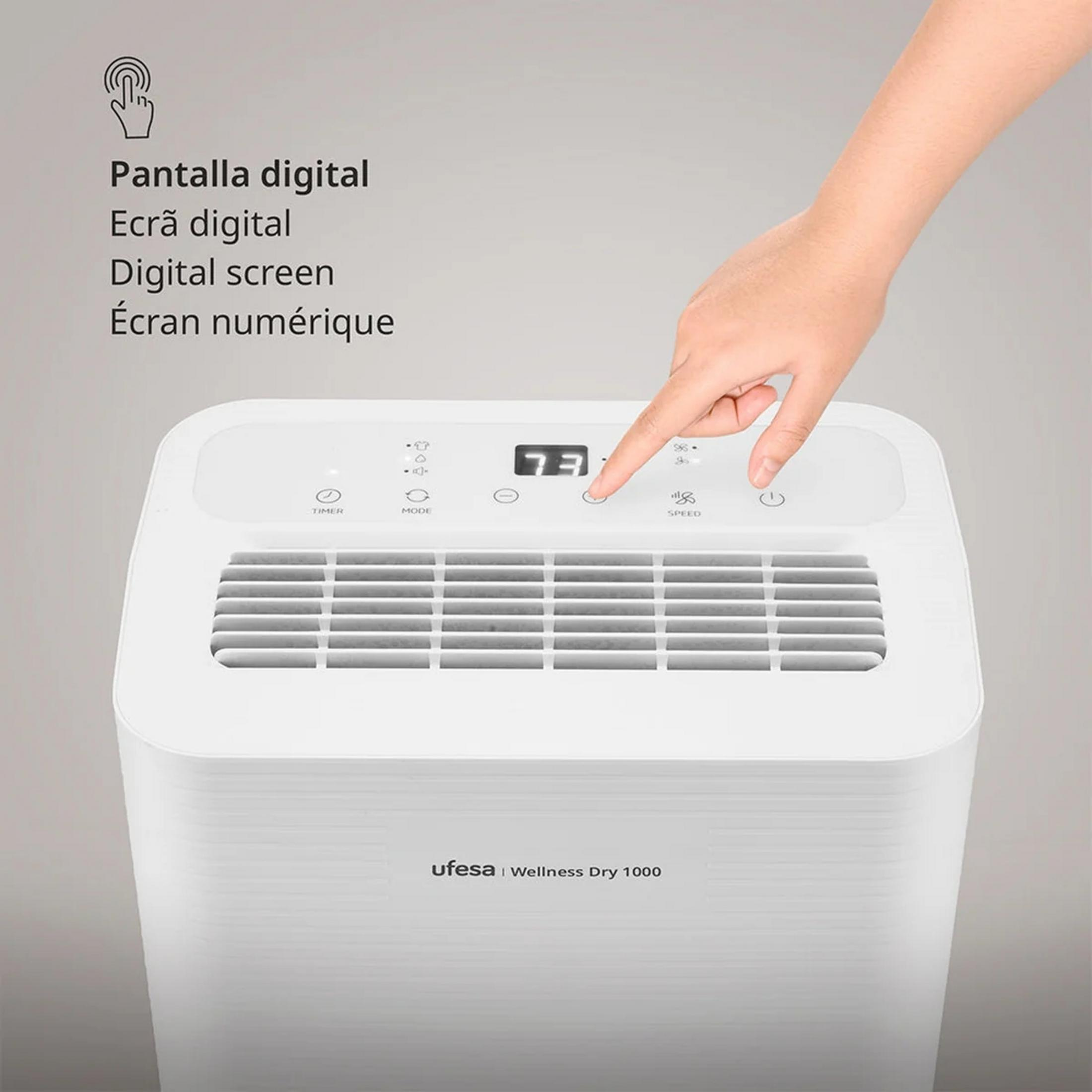 Una mano tocca il pulsante rotondo su un deumidificatore bianco con display.