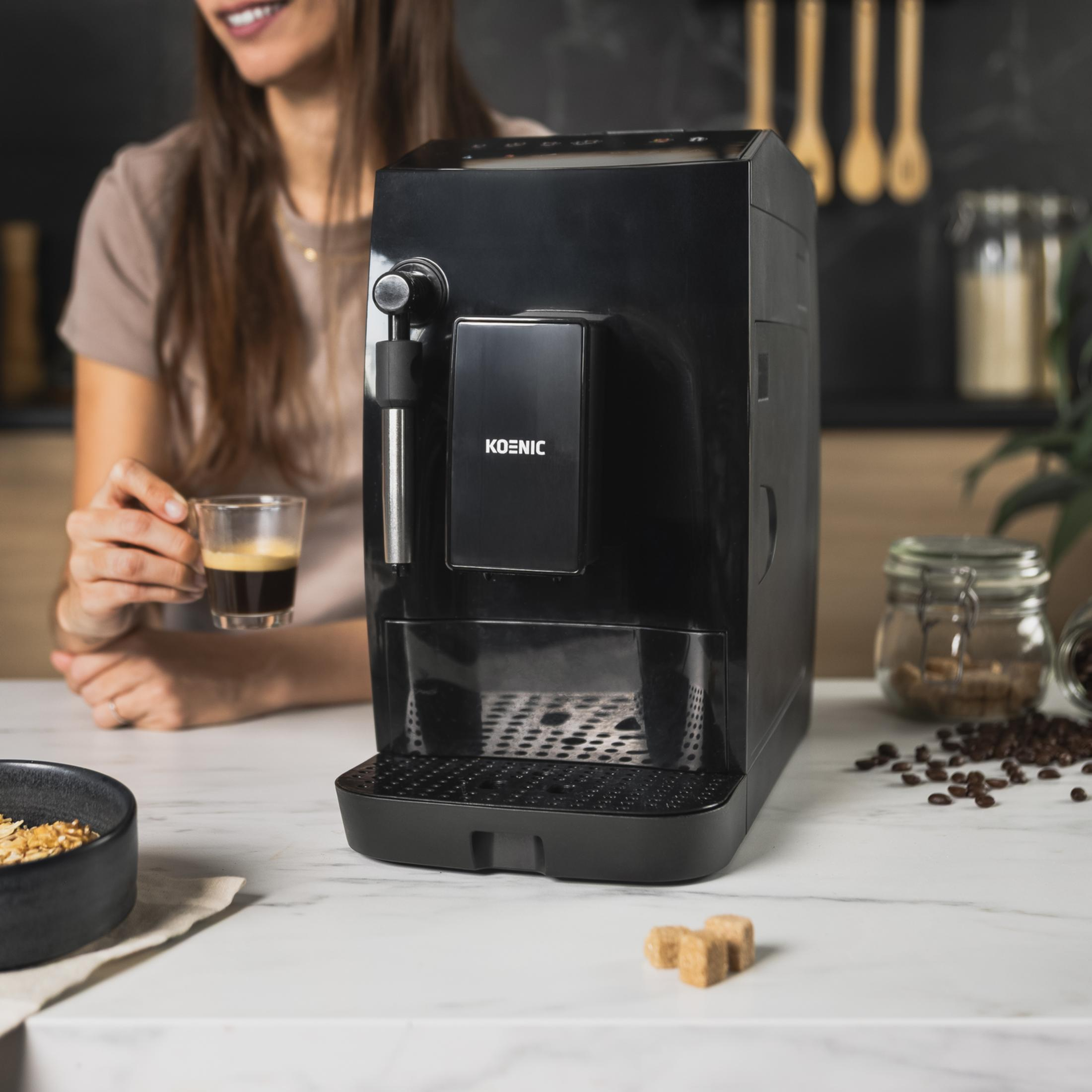Una mujer sostiene una taza de espresso junto a una cafetera negra.