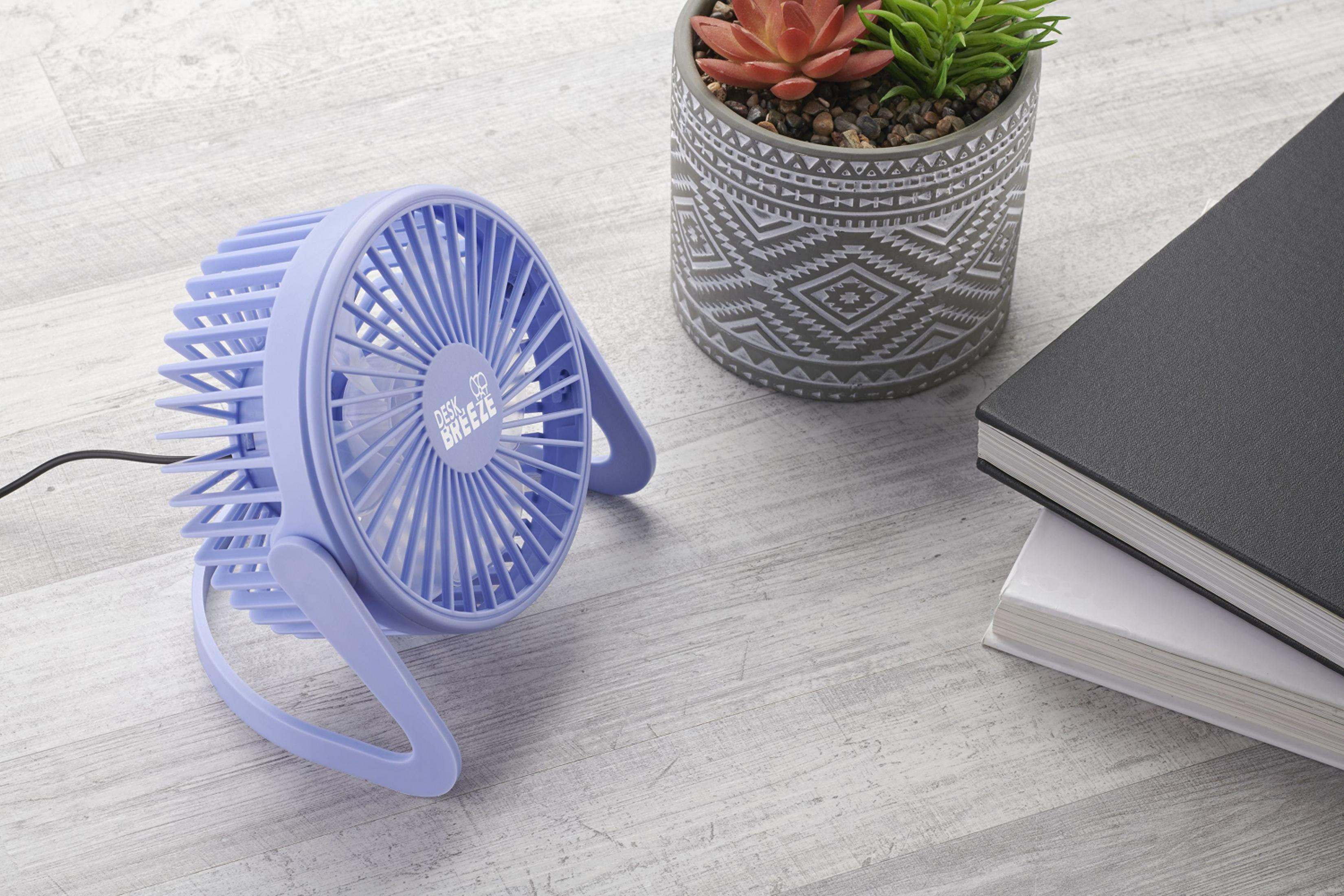 Un pequeño ventilador morado sobre un escritorio de madera junto a una suculenta en maceta y libros.