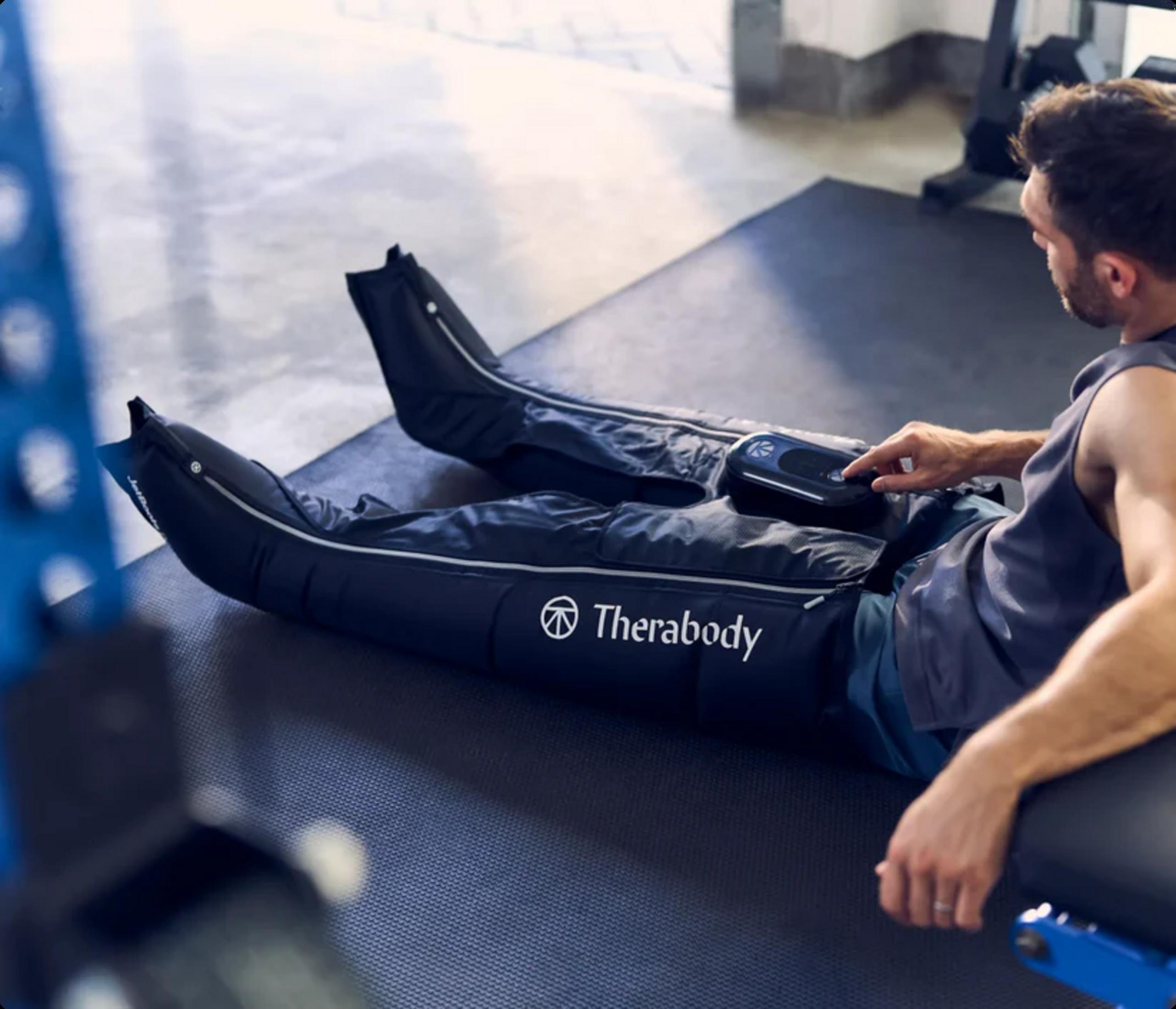 Un uomo usa un massaggiatore per gambe Therabody su un tappetino da palestra.