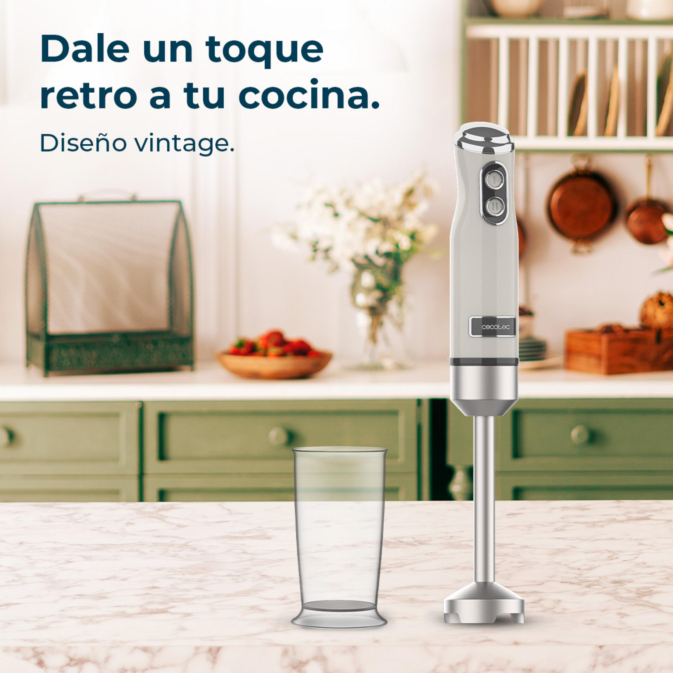 Un frullatore a immersione color crema con accenti argento accanto a un bicchiere.