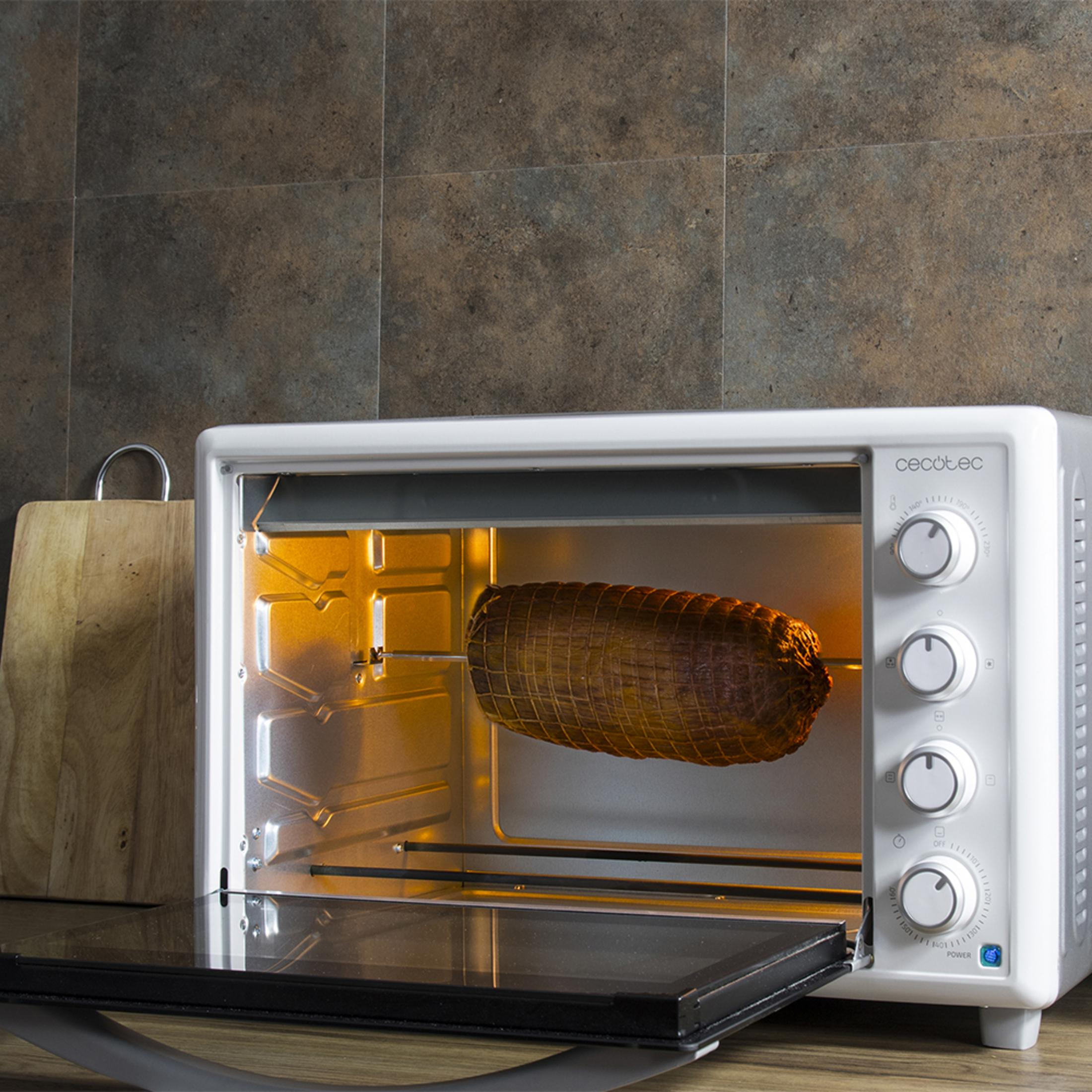 Un arrosto su uno spiedo cuoce in un forno bianco con la porta aperta.