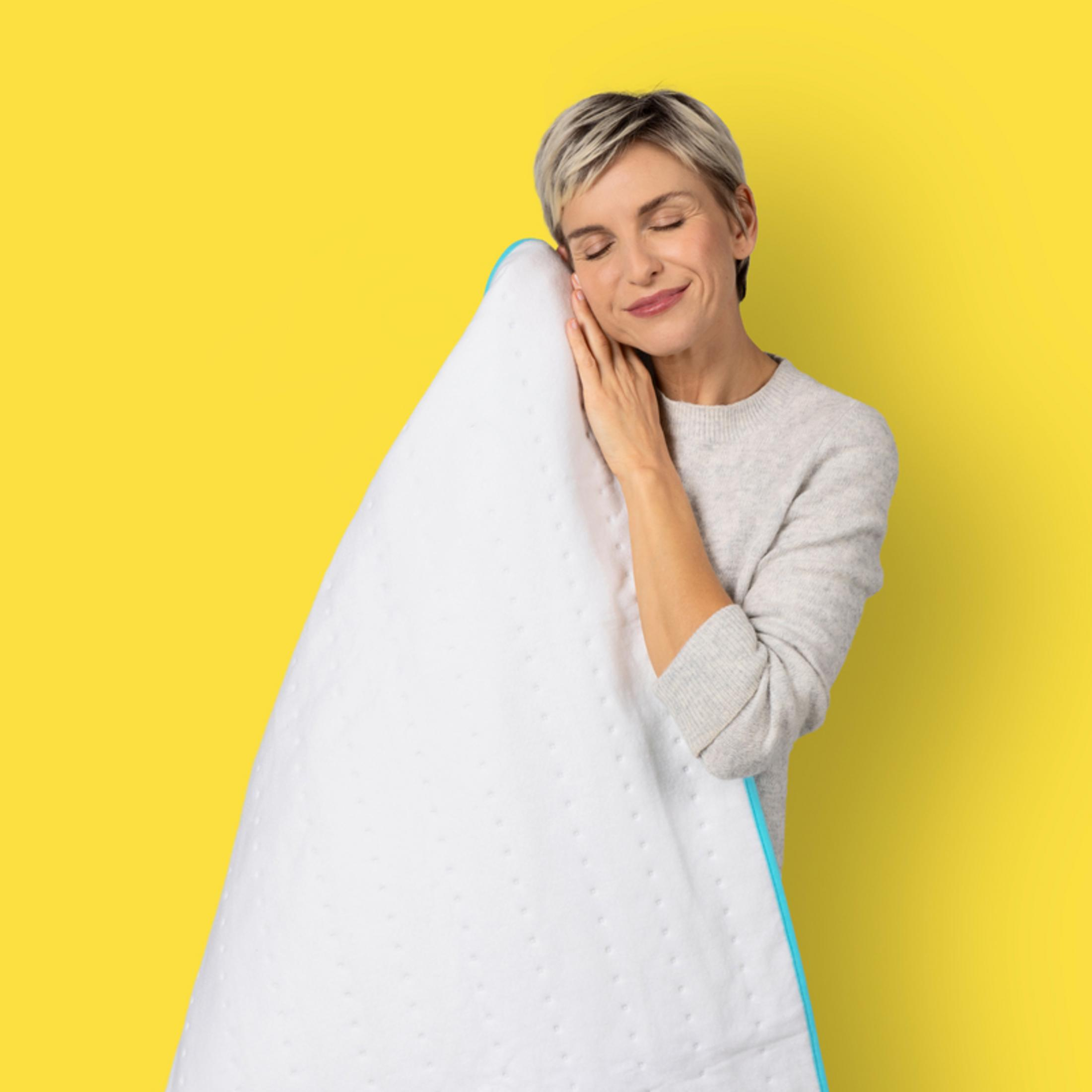 Mujer abrazando una almohada blanca sobre fondo amarillo.
