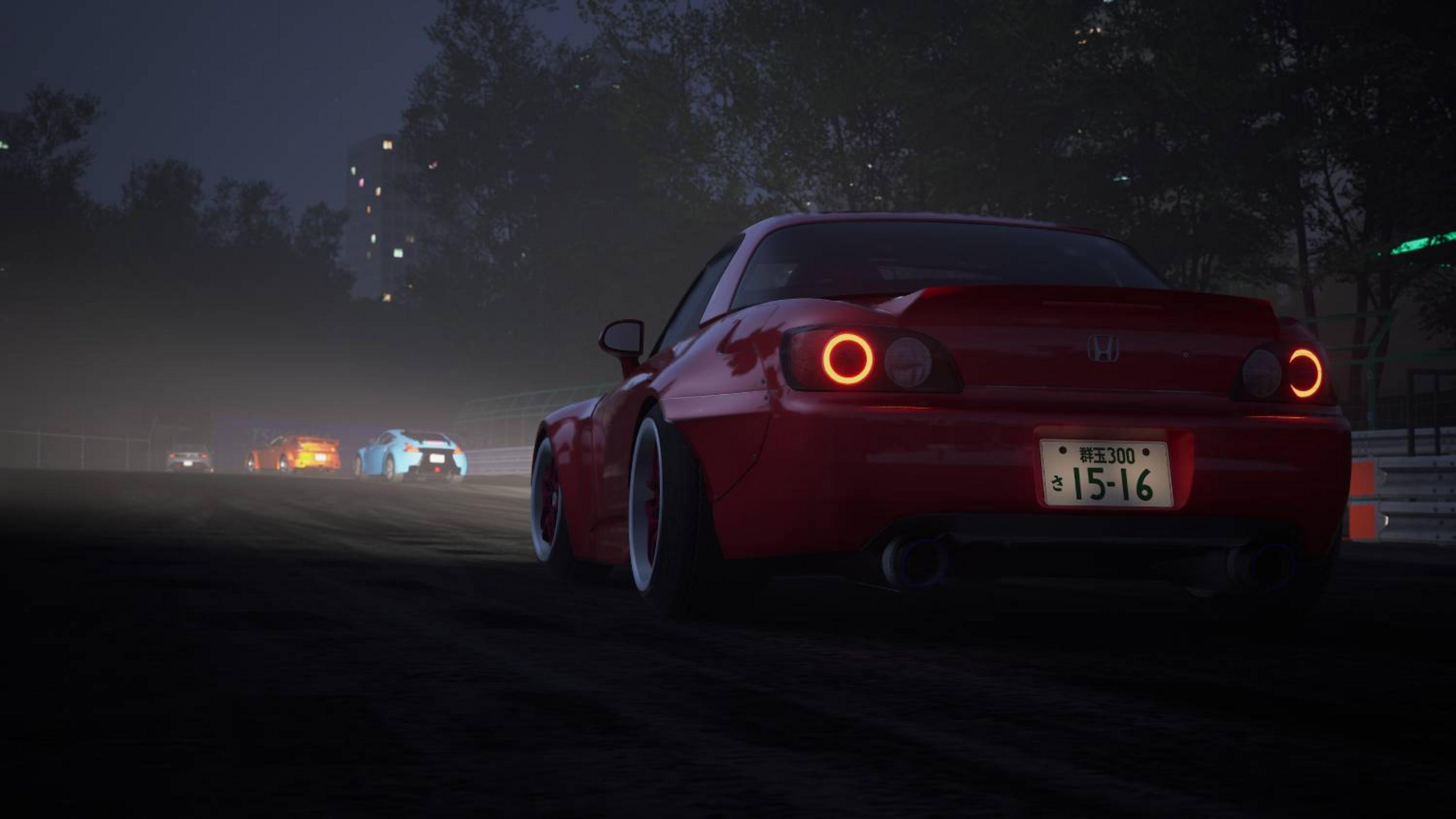 Auto sportiva rossa su pista da corsa di notte, altre auto nella nebbia.