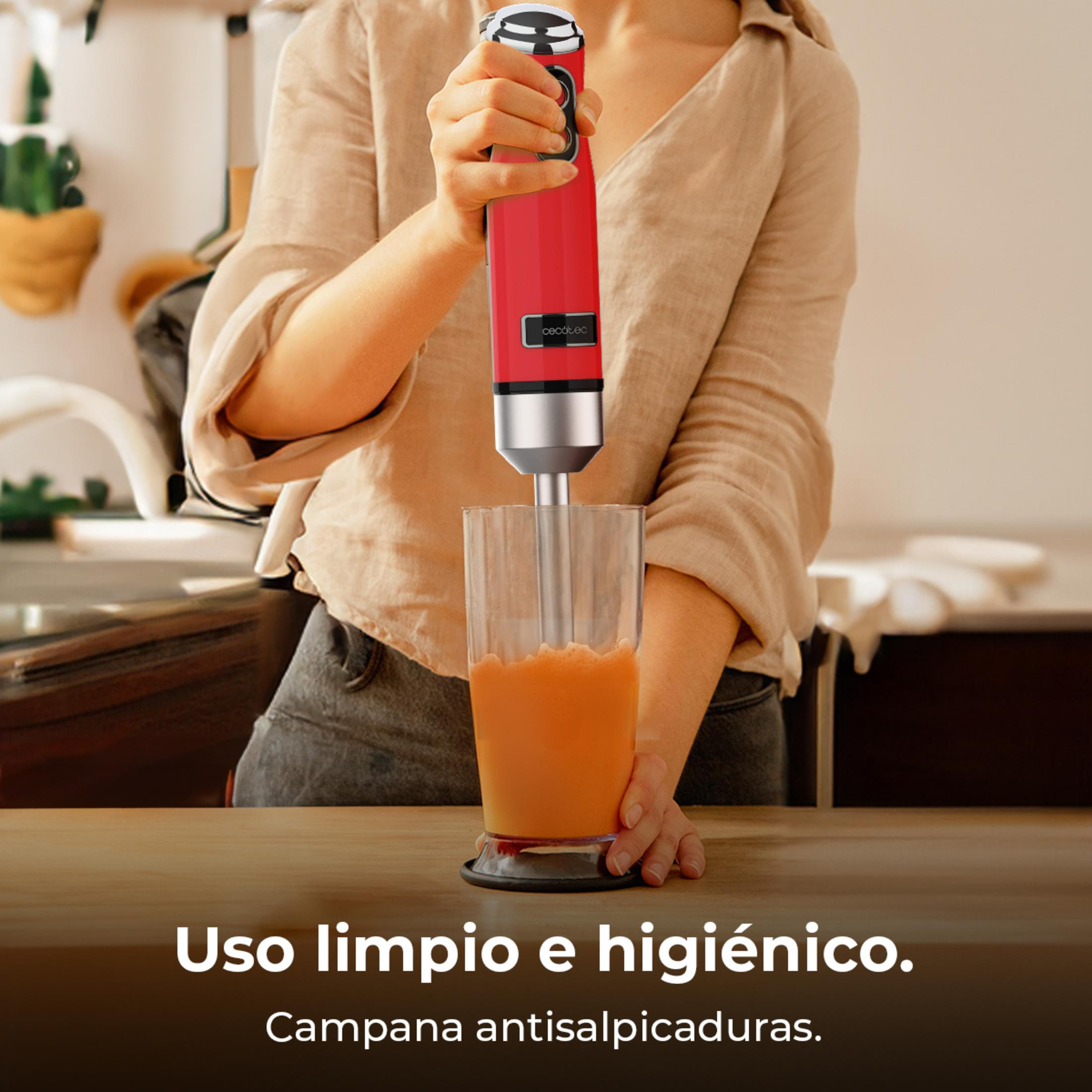 Eine Person mixt mit einem roten Stabmixer in einem Glas Orangensaft.