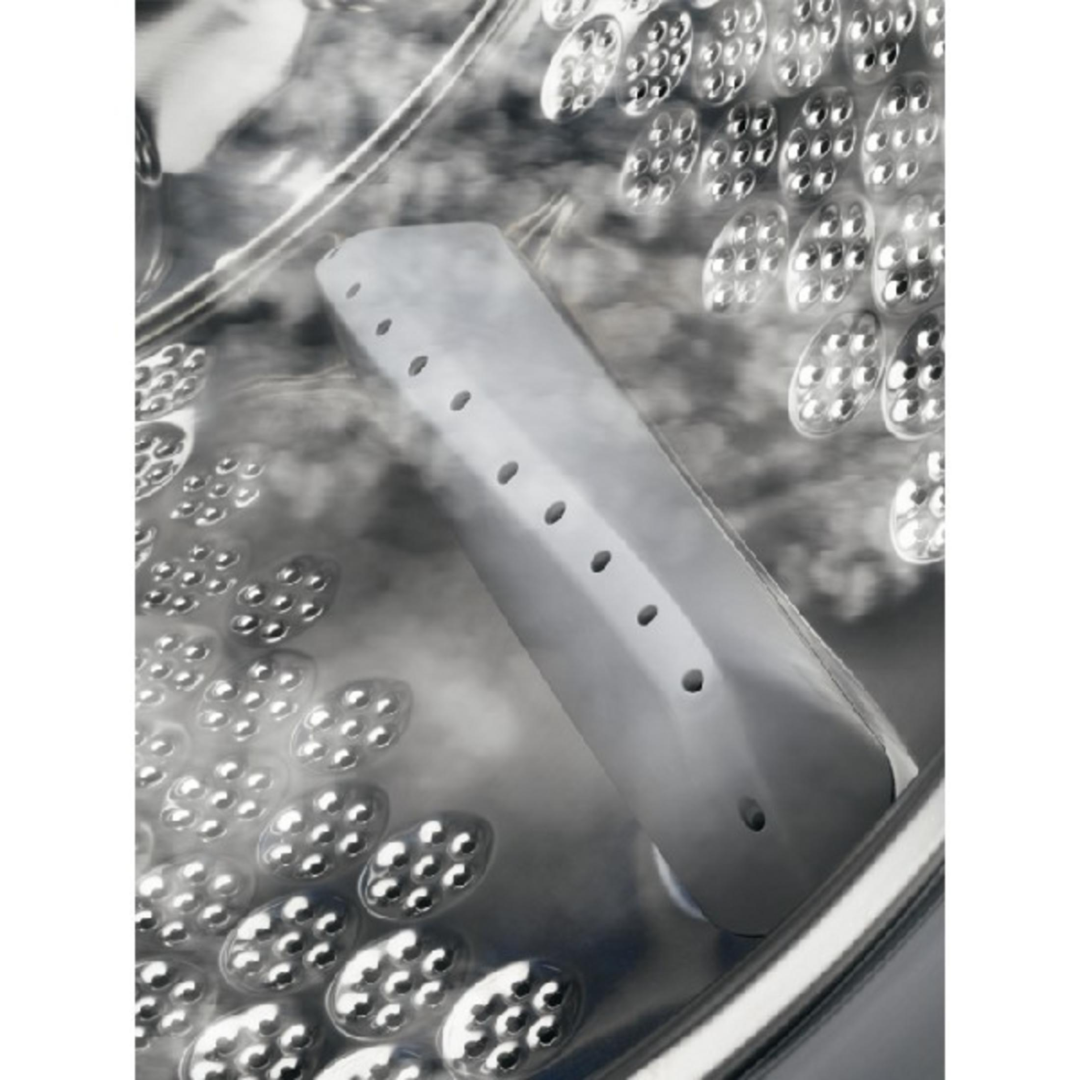 El vapor sale dentro del tambor de una lavadora, con una boquilla de vapor gris con agujeros.