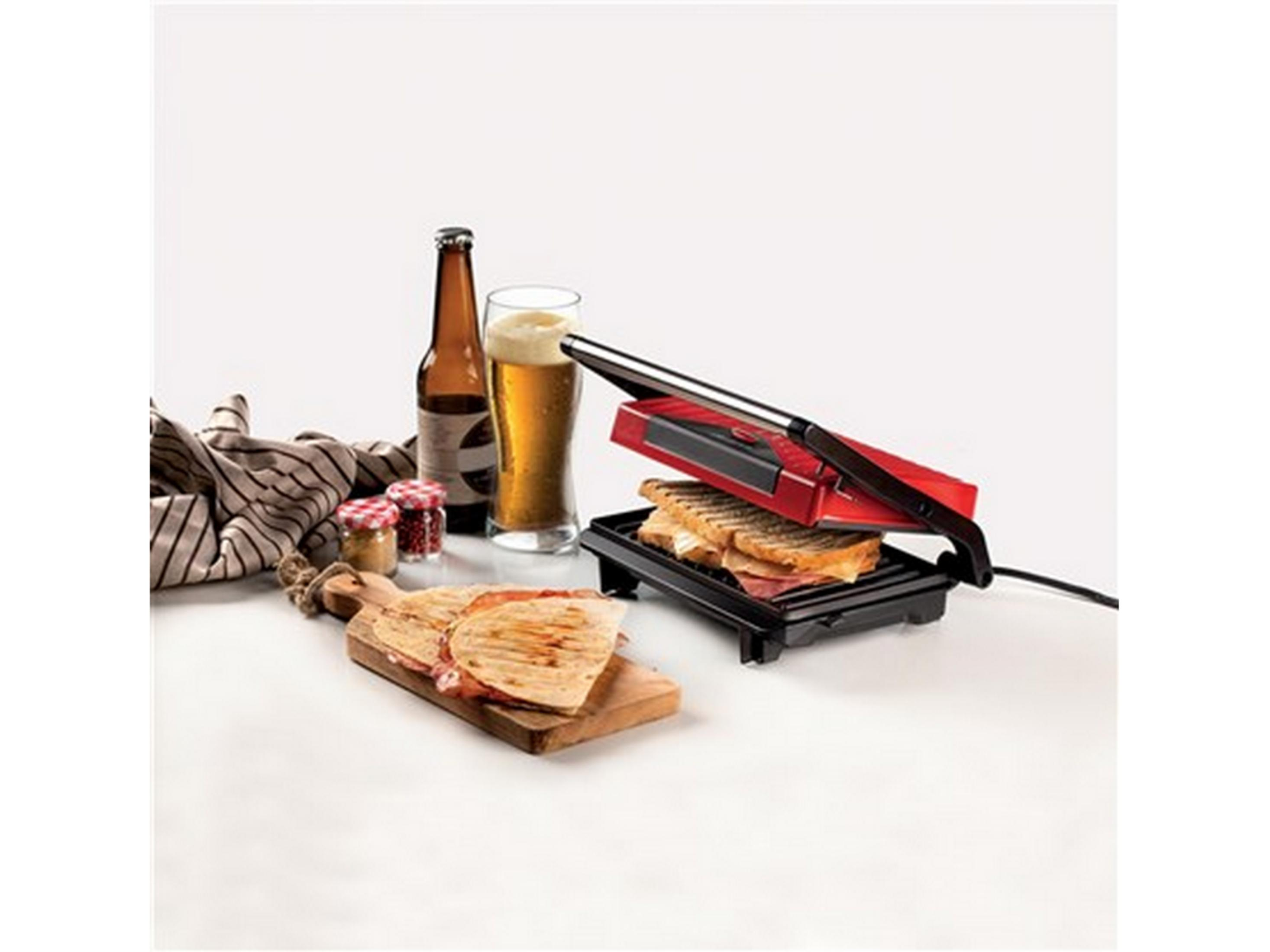 Una sandwichera roja con sándwiches, cerveza y especias en una mesa de madera.