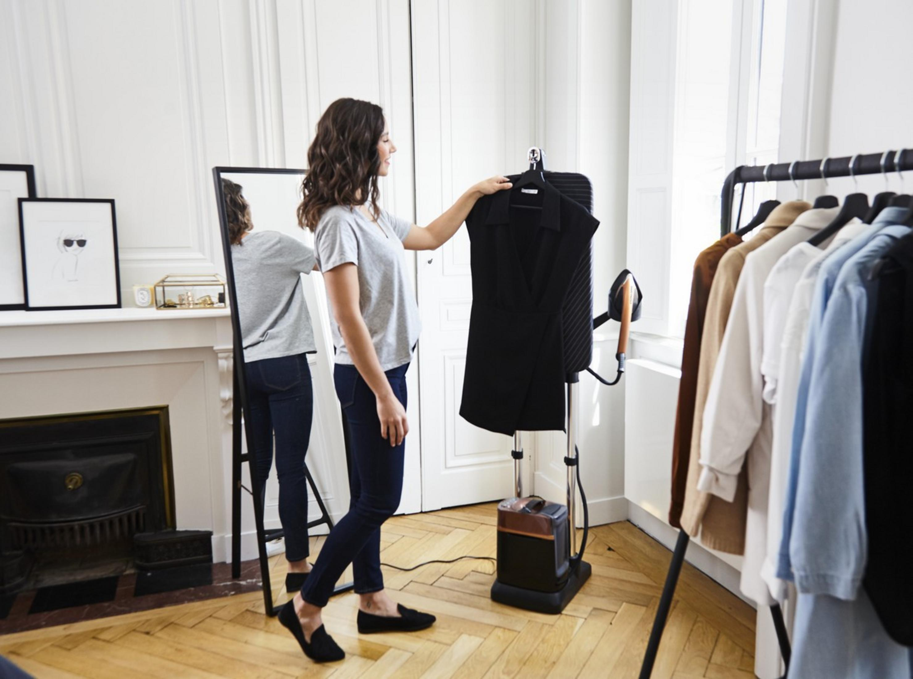 Una donna in t-shirt grigia e jeans blu stira un capo nero.