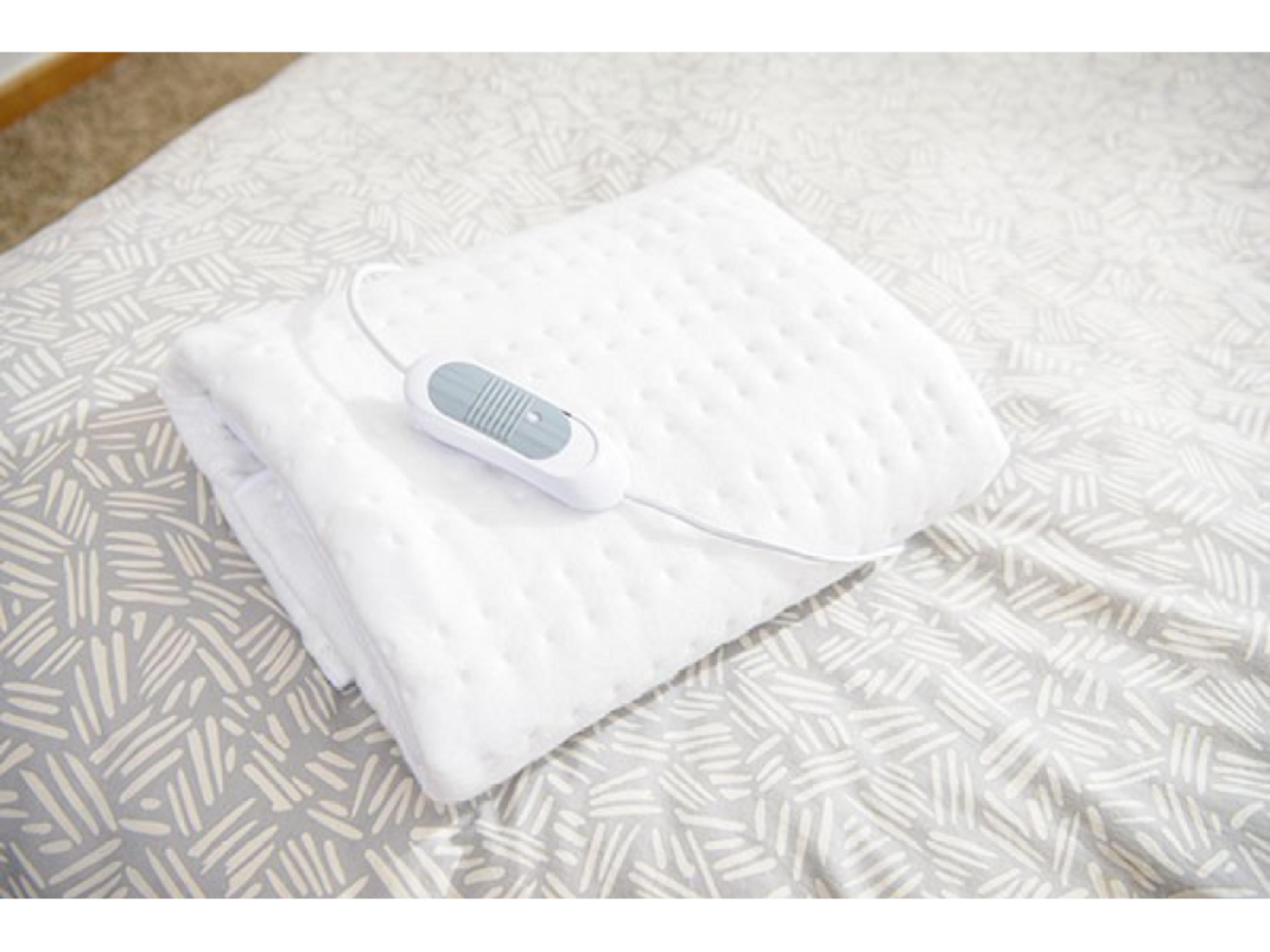 A folded white electric blanket with a controller lies on a patterned duvet.