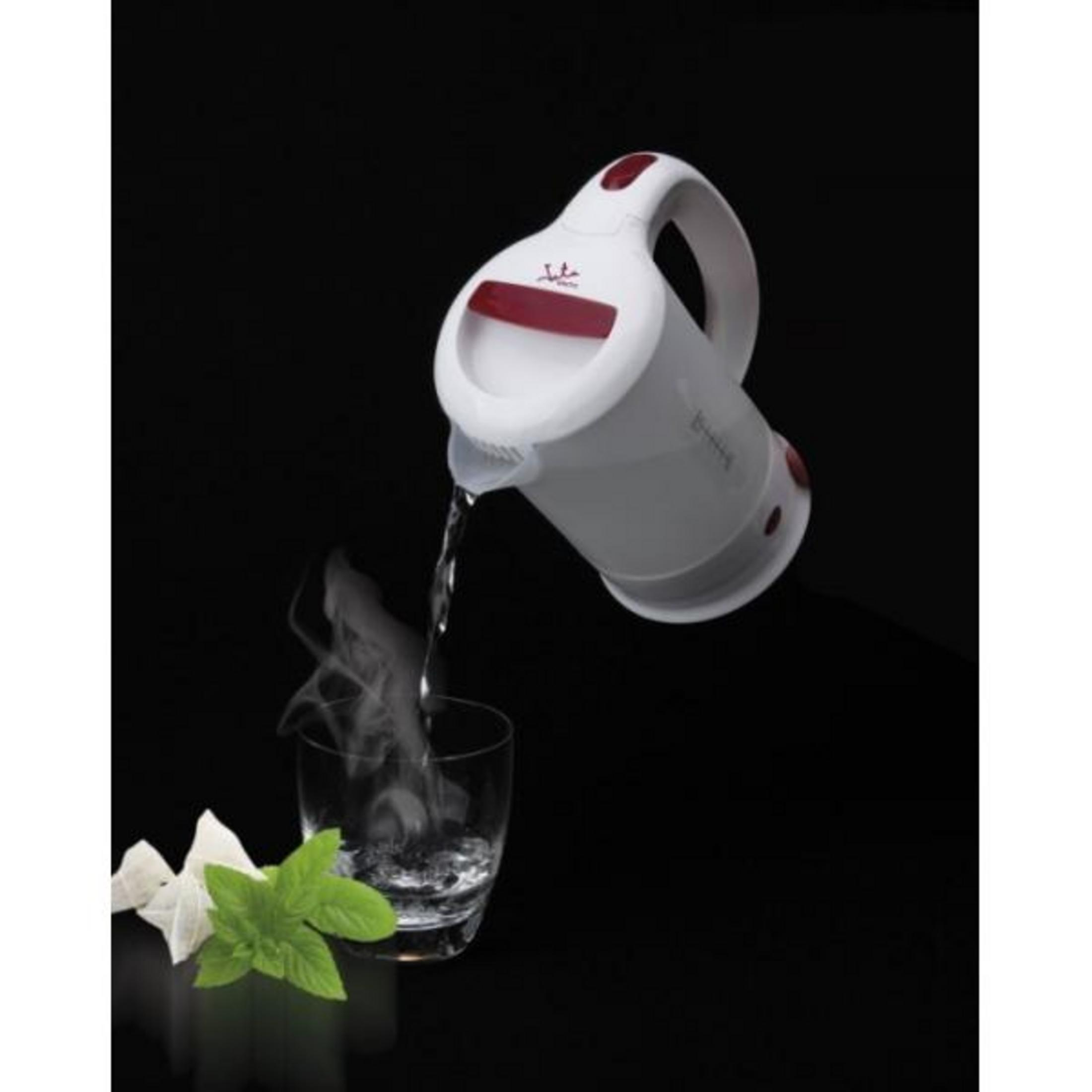 Una tetera blanca vierte agua caliente en un vaso con vapor y menta.
