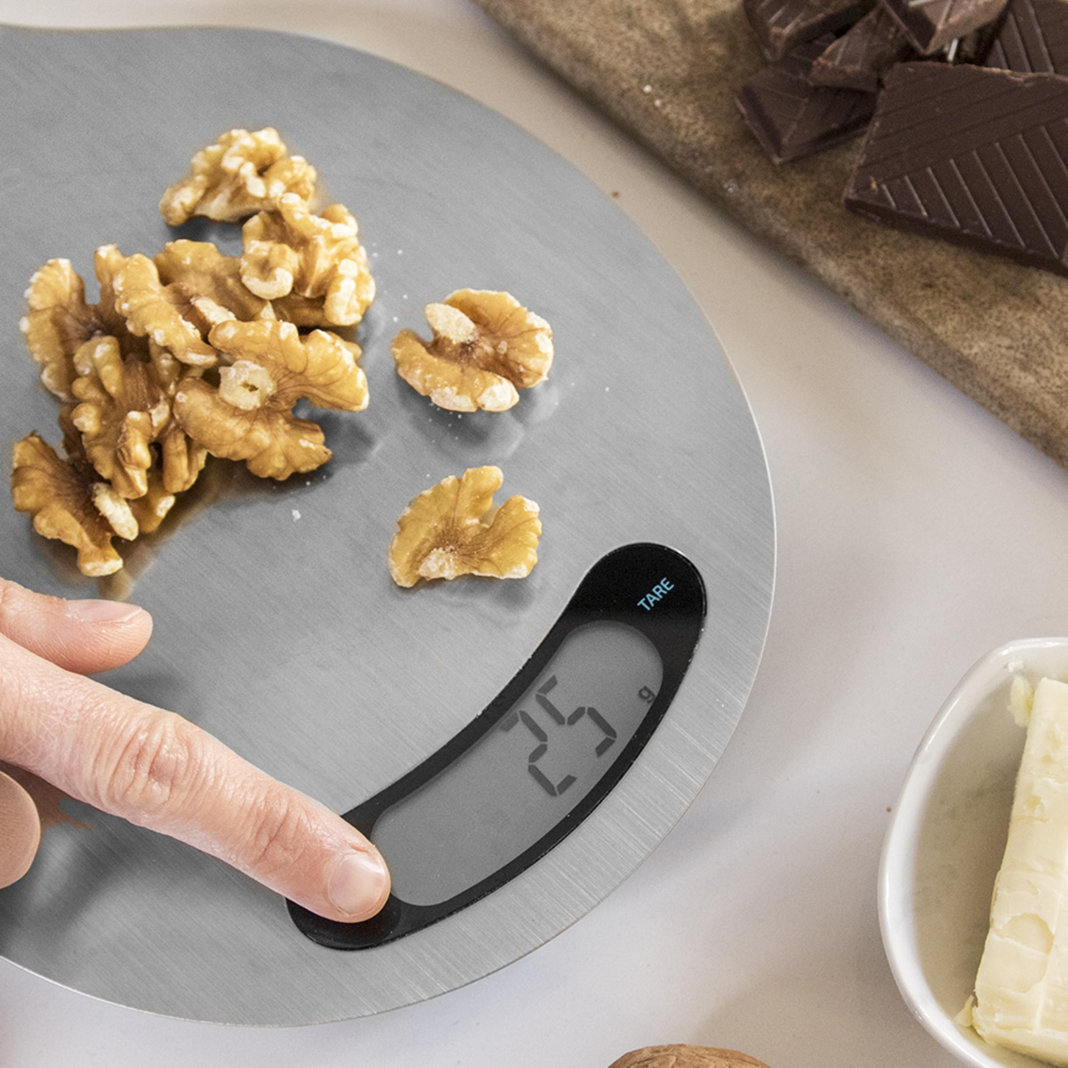 Walnuts are being weighed on a digital scale. Chocolate and butter are nearby.