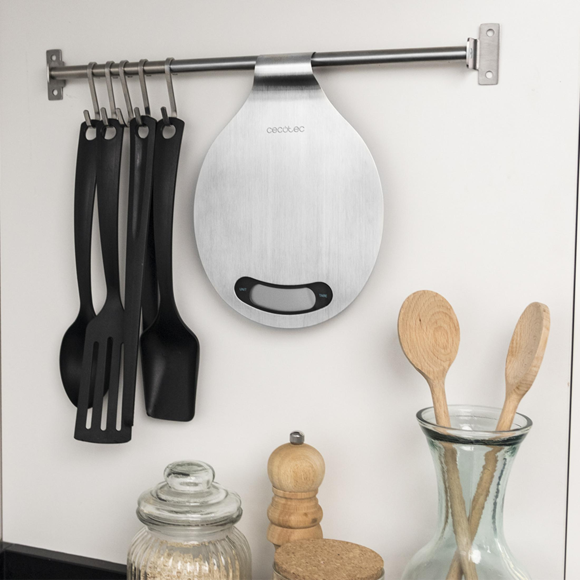 Kitchen scale hanging on wall with utensils. Wooden spoons in vase.