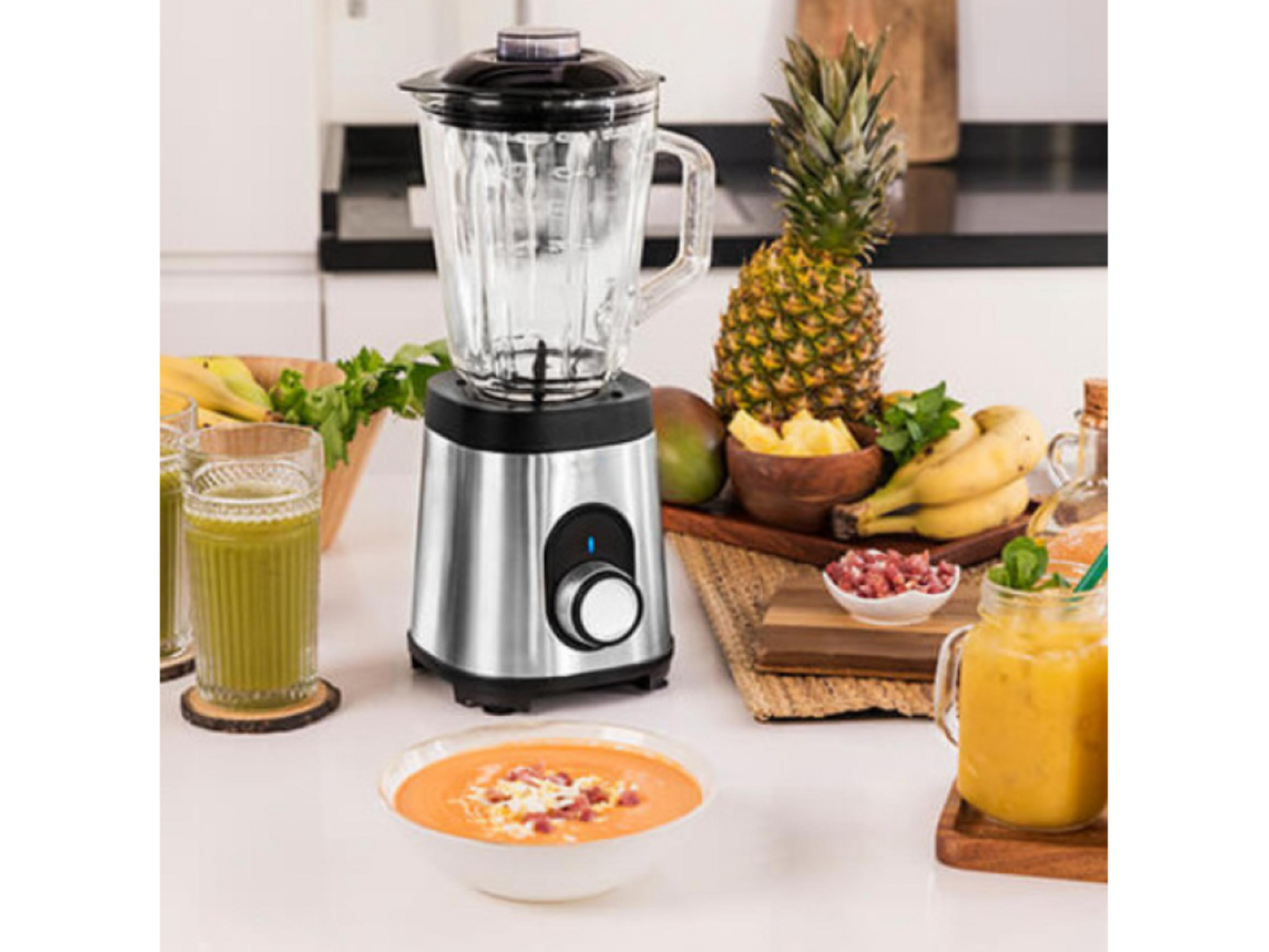 Un frullatore argento con caraffa in vetro accanto a frutta e frullati.