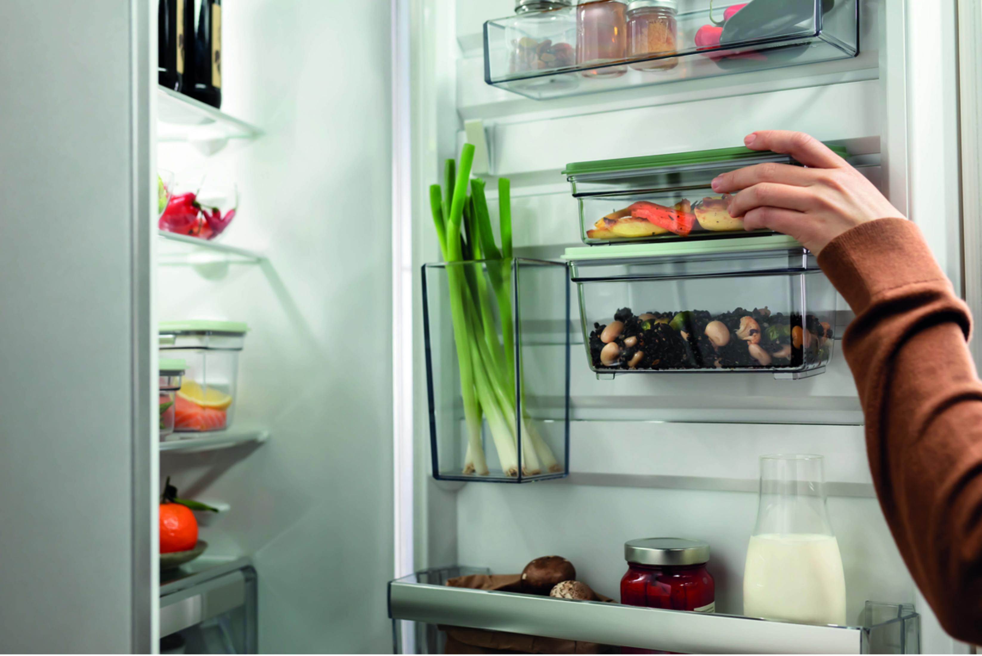 Una mano cierra un recipiente con comida en el refrigerador.