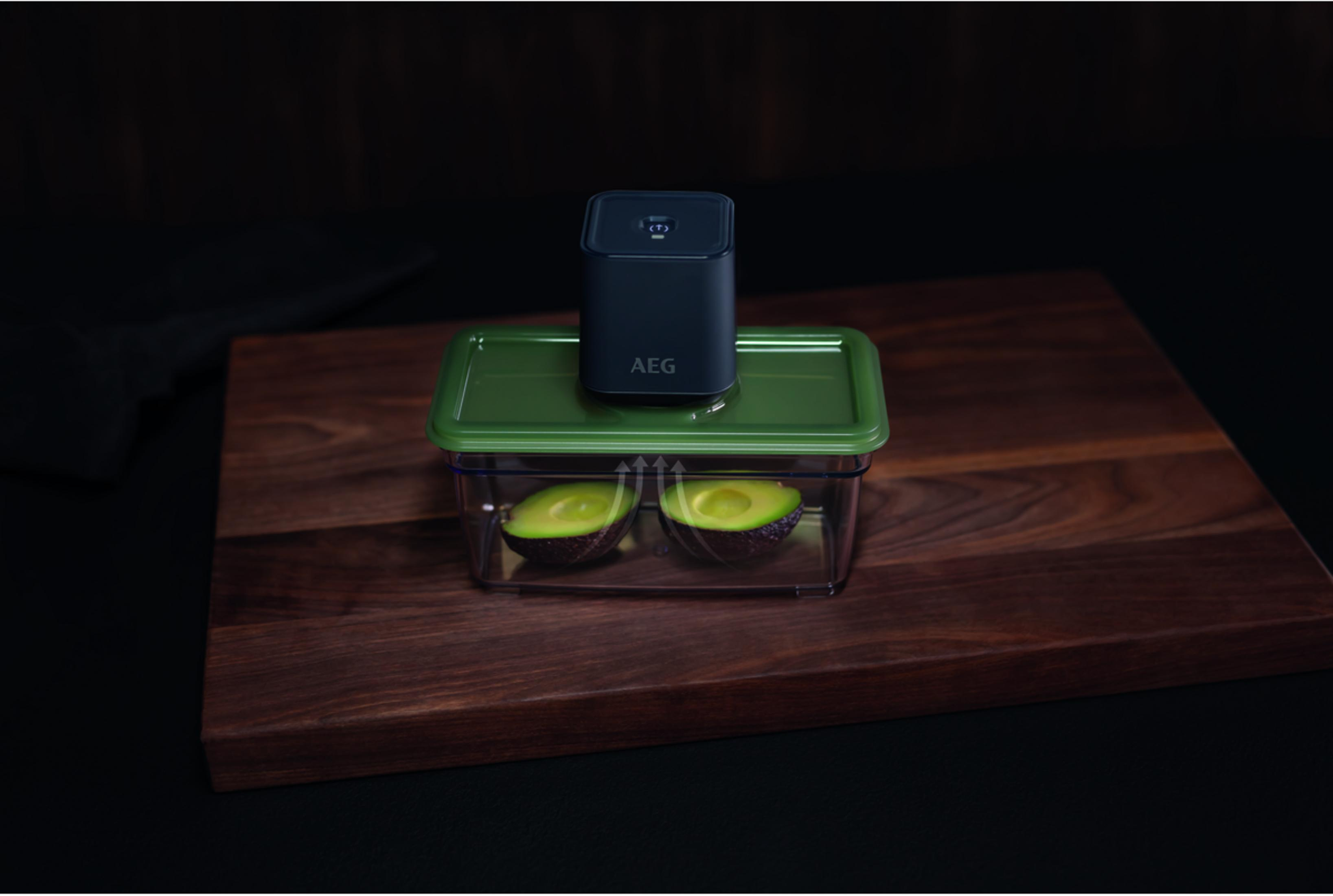 Un sellador al vacío negro se asienta sobre una tapa verde sobre aguacates en un recipiente.
