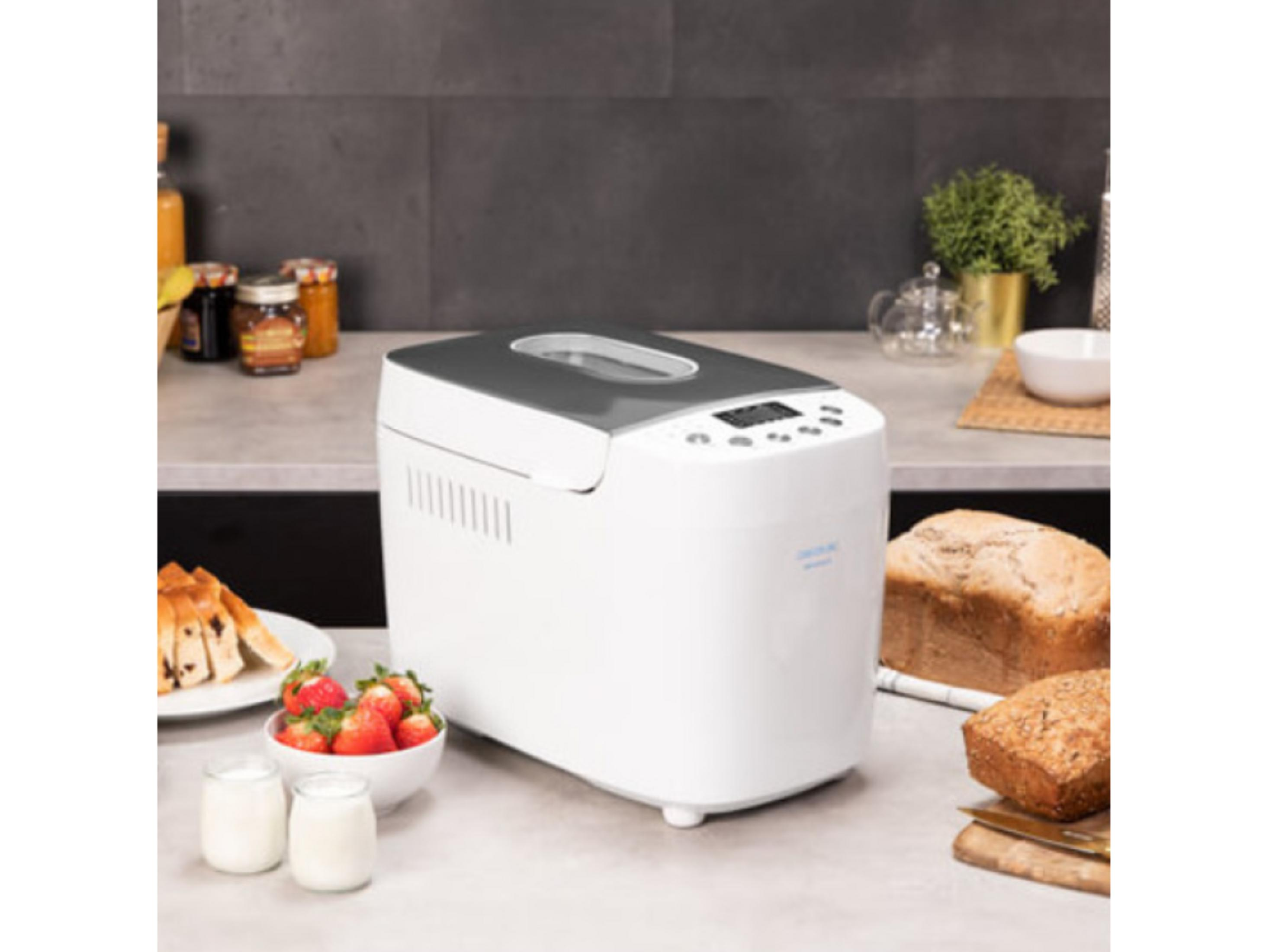 Ein weißer Brotbackautomat steht auf einer Arbeitsplatte mit Brot, Erdbeeren und Joghurt.