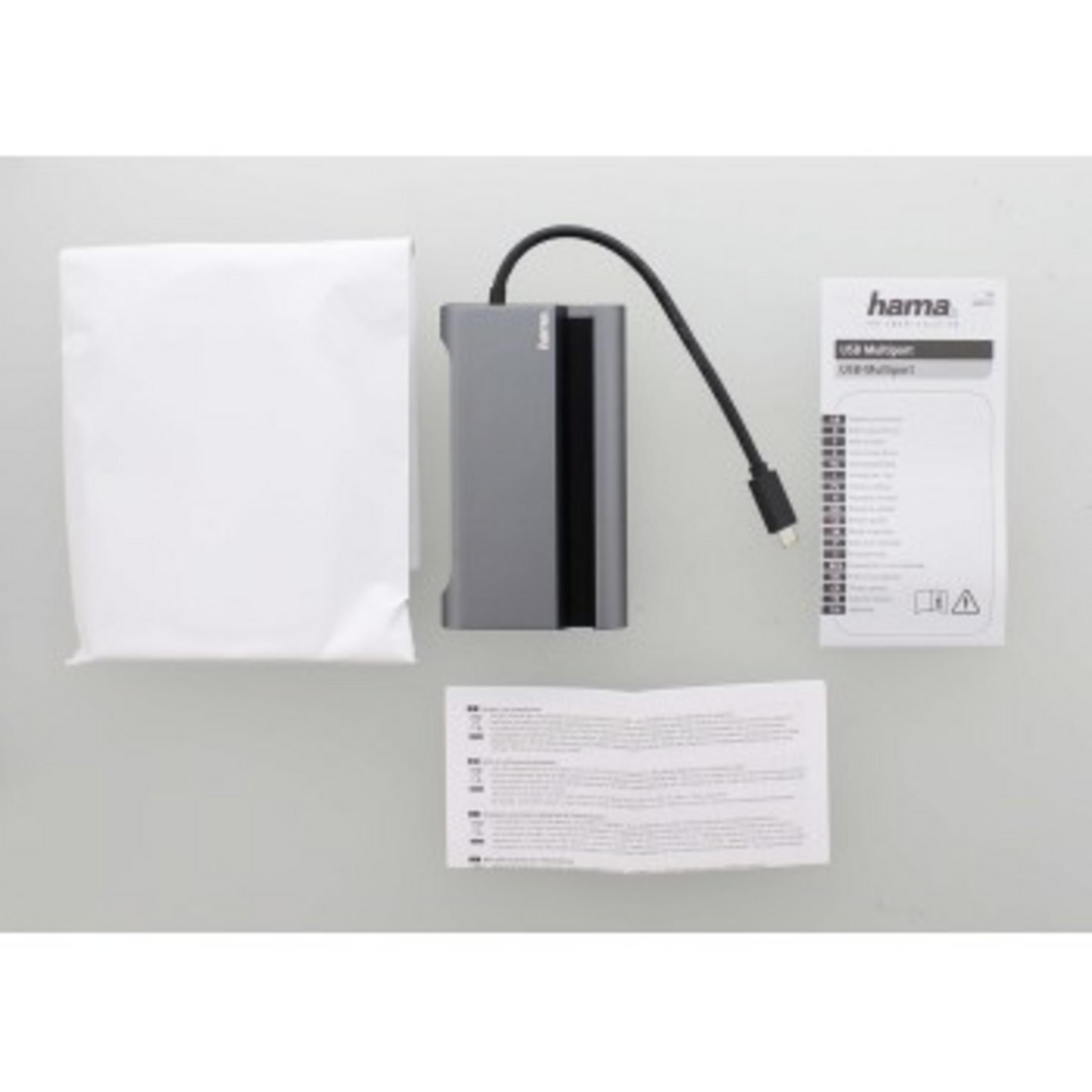 Hub USB-C grigio con cavo, sacchetto bianco e manuale su sfondo grigio.