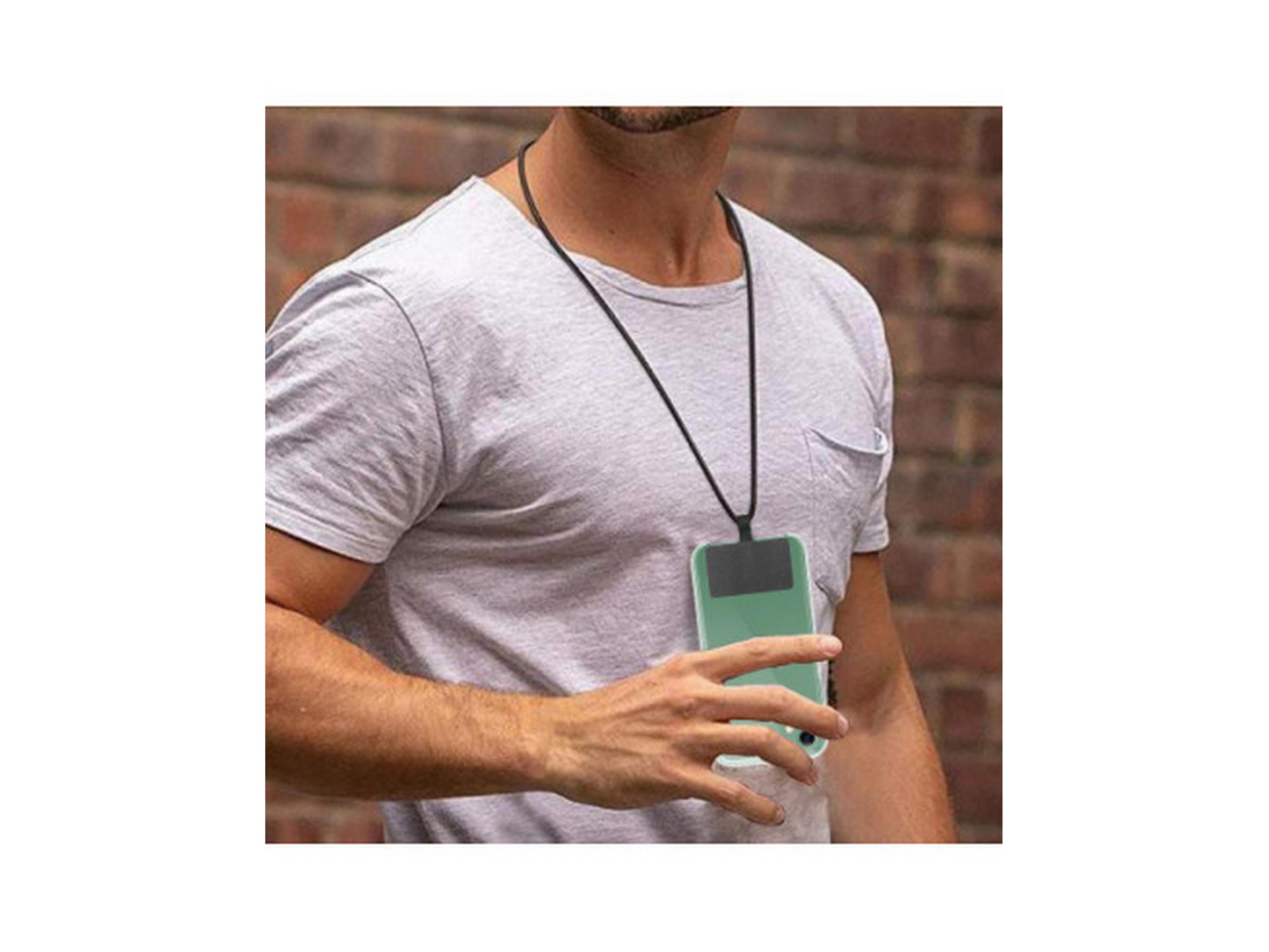 Hombre con camiseta gris lleva un smartphone con cordón, fondo de pared de ladrillos.