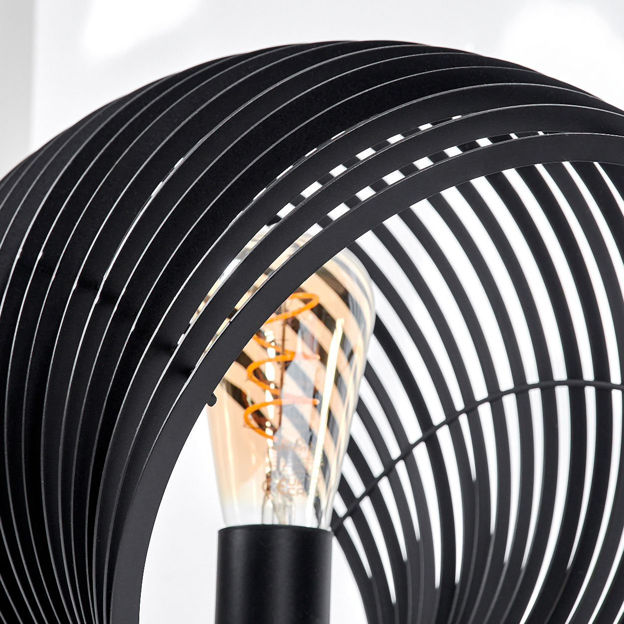 Eine schwarze Lampe mit einer sichtbaren Glühbirne und einem spiralförmigen Design.