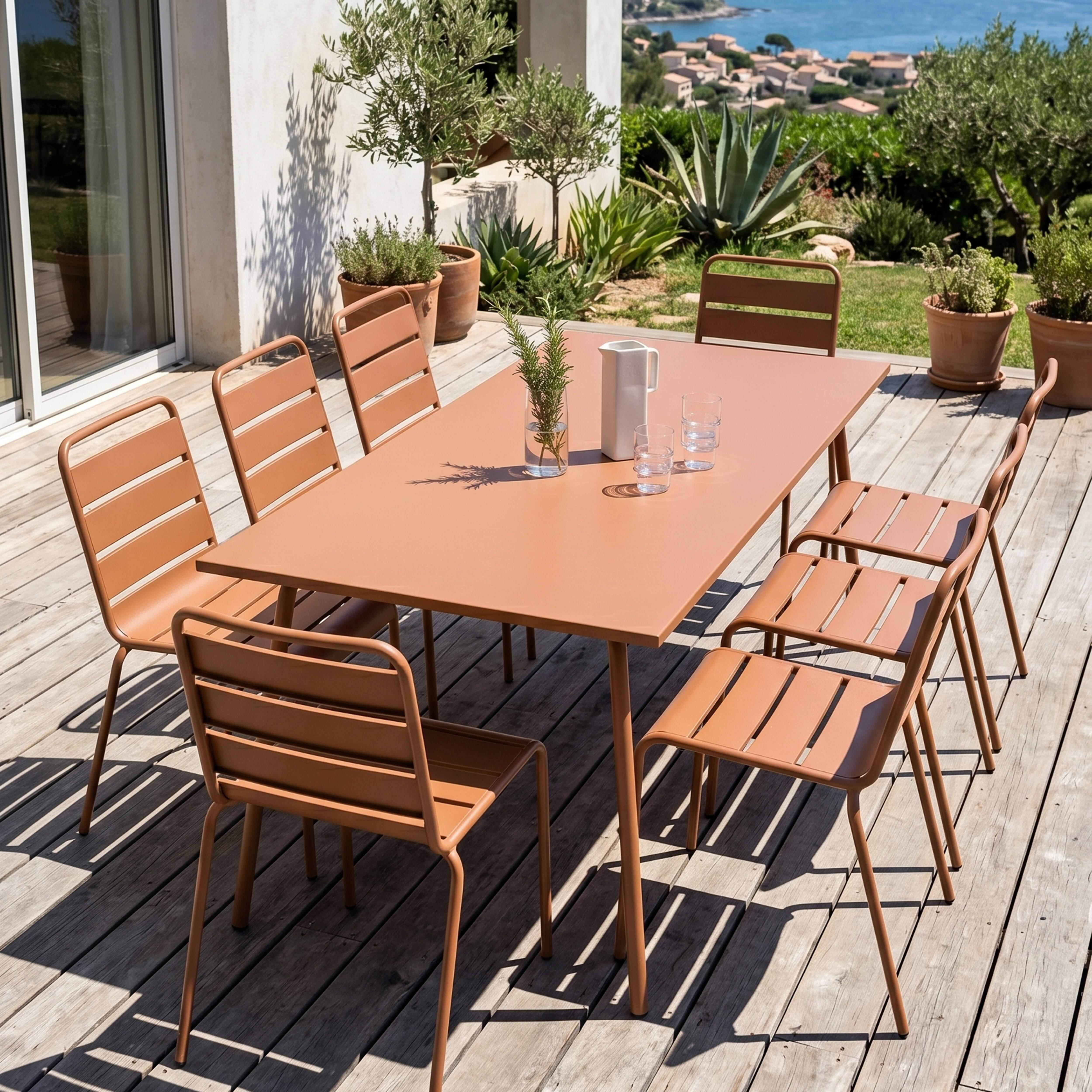 Ein brauner Gartentisch mit Stühlen auf einer Holzterrasse mit Blick auf das Meer.