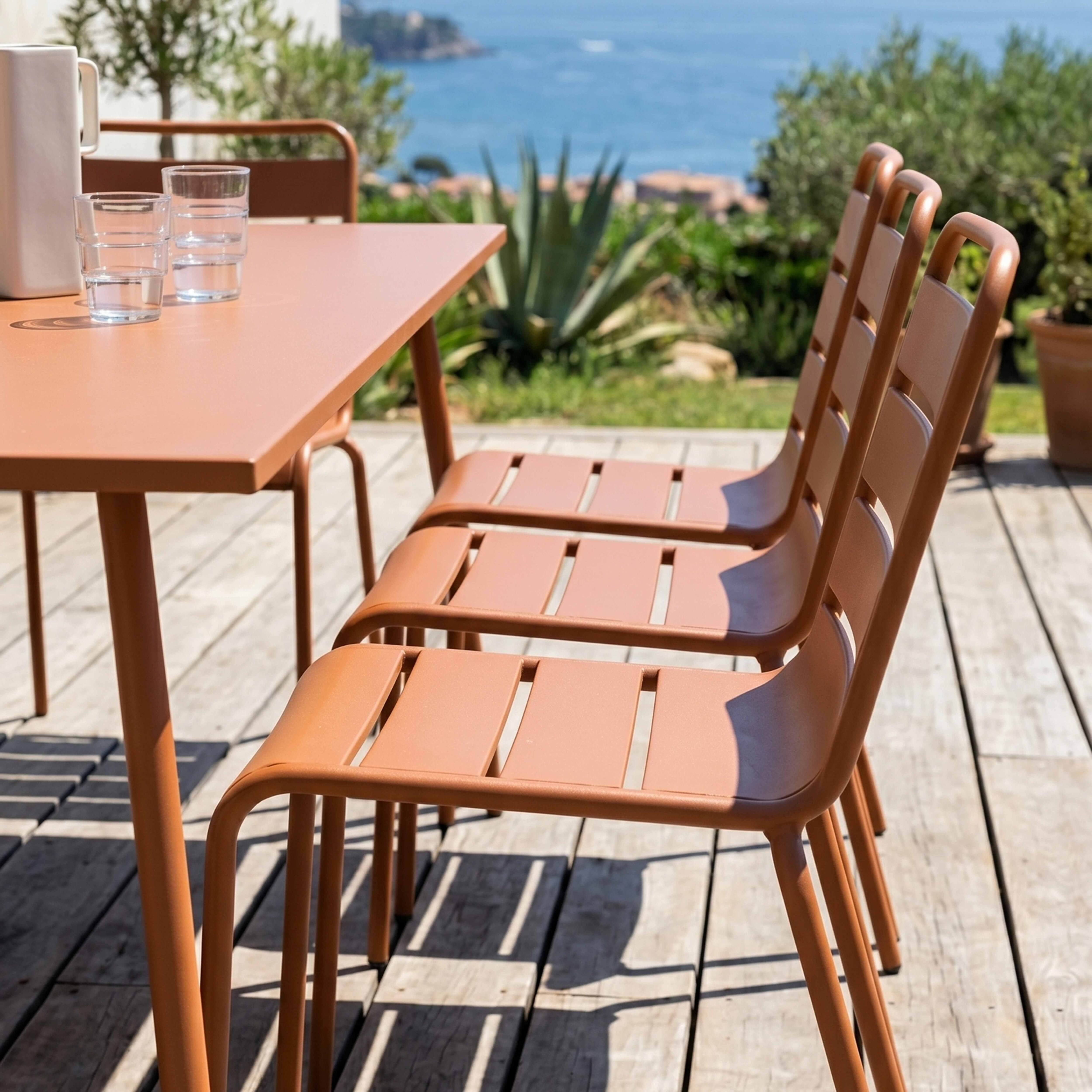 Ein orangefarbener Tisch und vier Stühle stehen auf einer Holzterrasse am Meer.