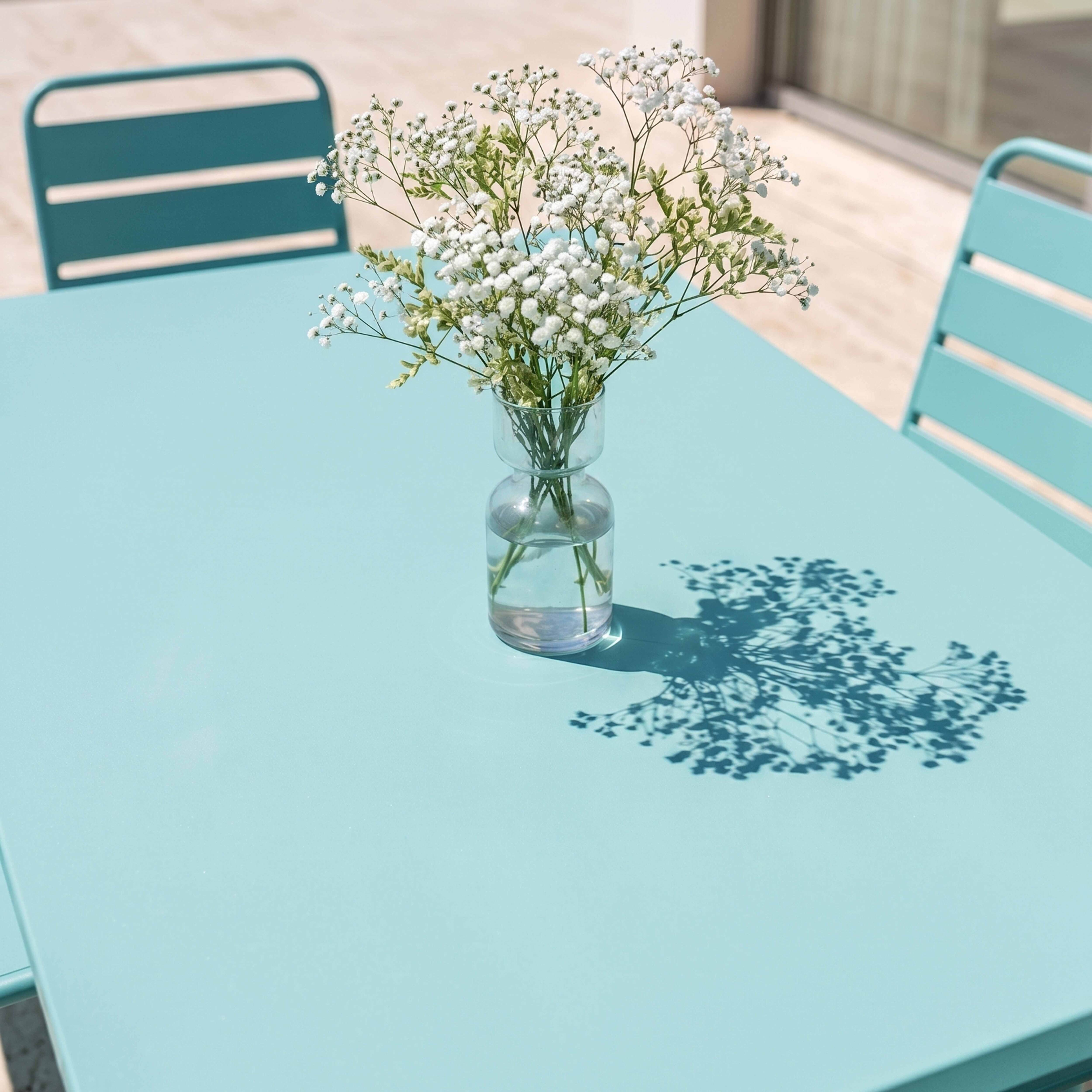 Ein Strauß Gänseblümchen in einer Glasvase auf einem hellblauen Tisch.