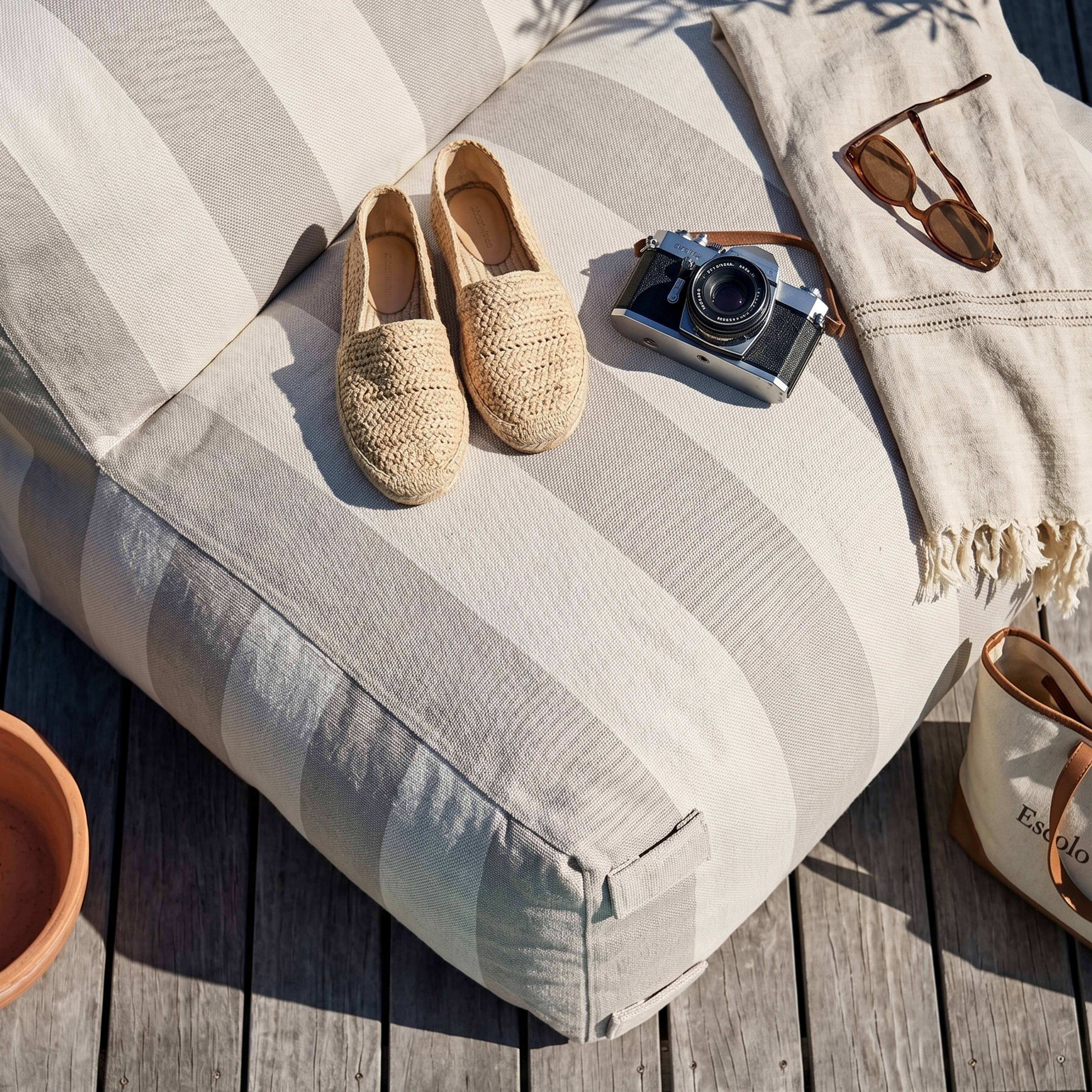 Geflochtene Espadrilles, Kamera, Sonnenbrille und Tasche auf einem gestreiften Kissen.