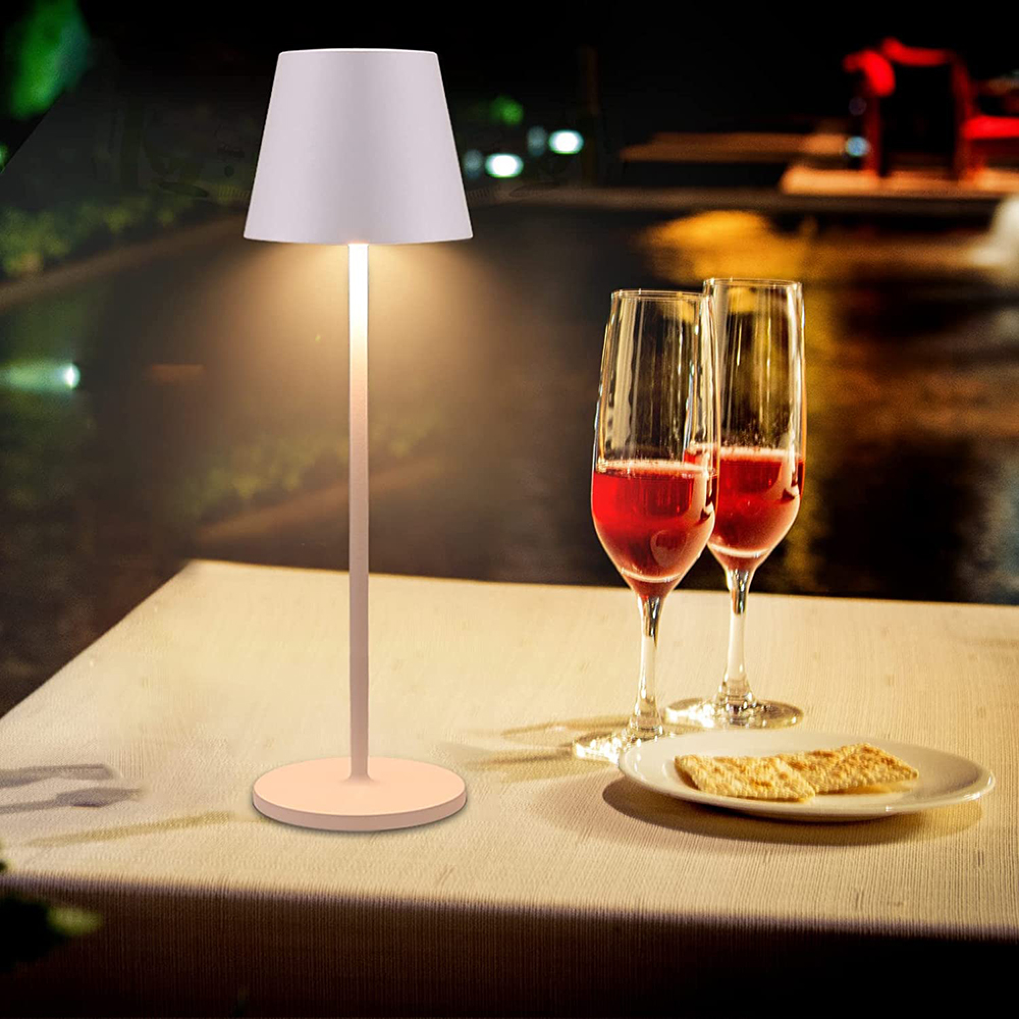Ein Tisch mit zwei Weingläsern, Keksen und einer Lampe bei Nacht.