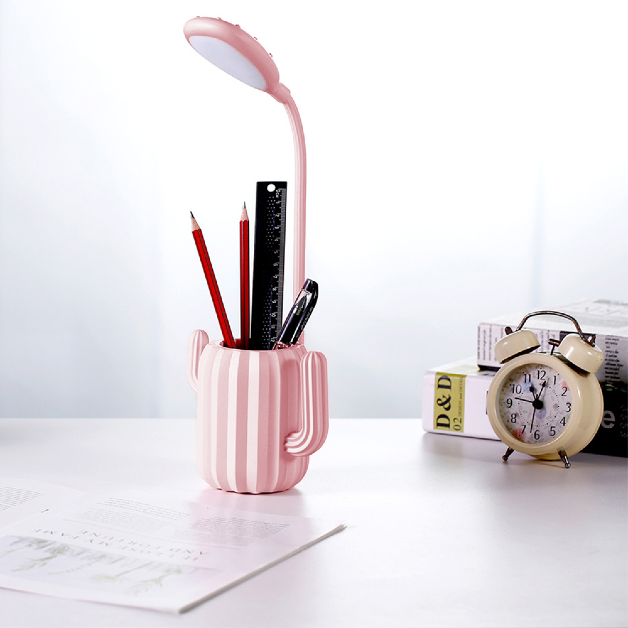 Ein rosa Kaktus-Stiftehalter mit Bleistiften, einem Lineal, einem Stift und einer Lampe.