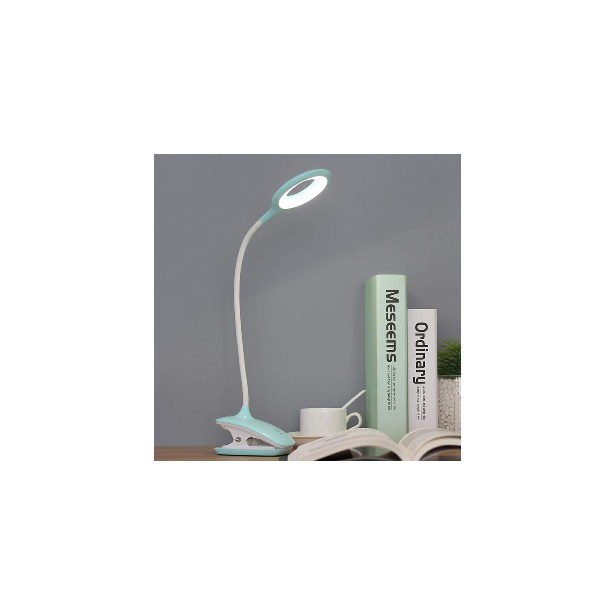 Eine blaue Klemmlampe leuchtet neben Büchern und einer Tasse auf einem Schreibtisch.