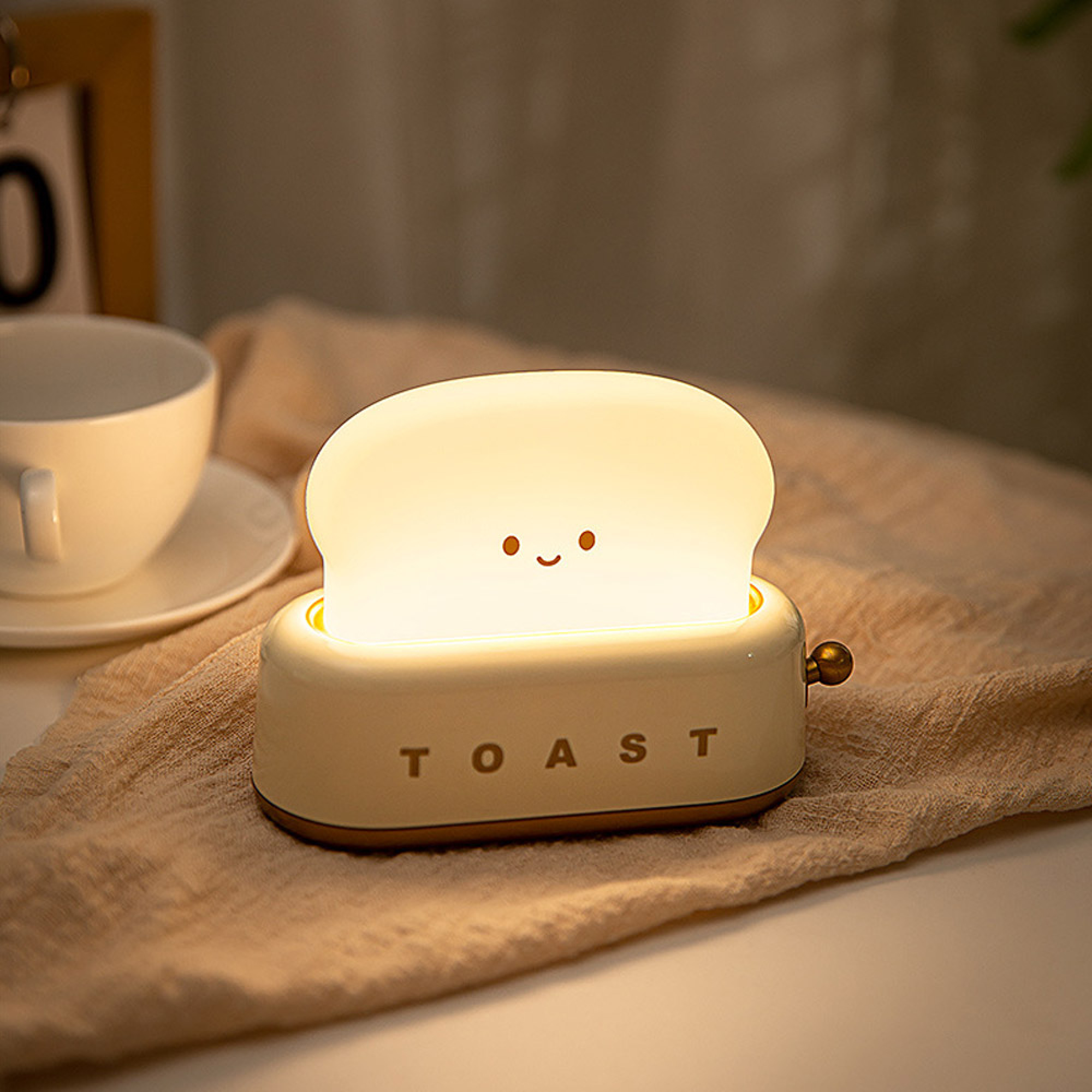 Ein niedlicher Toaster-Nachtlicht mit süßem Gesicht leuchtet auf einem Stoff.