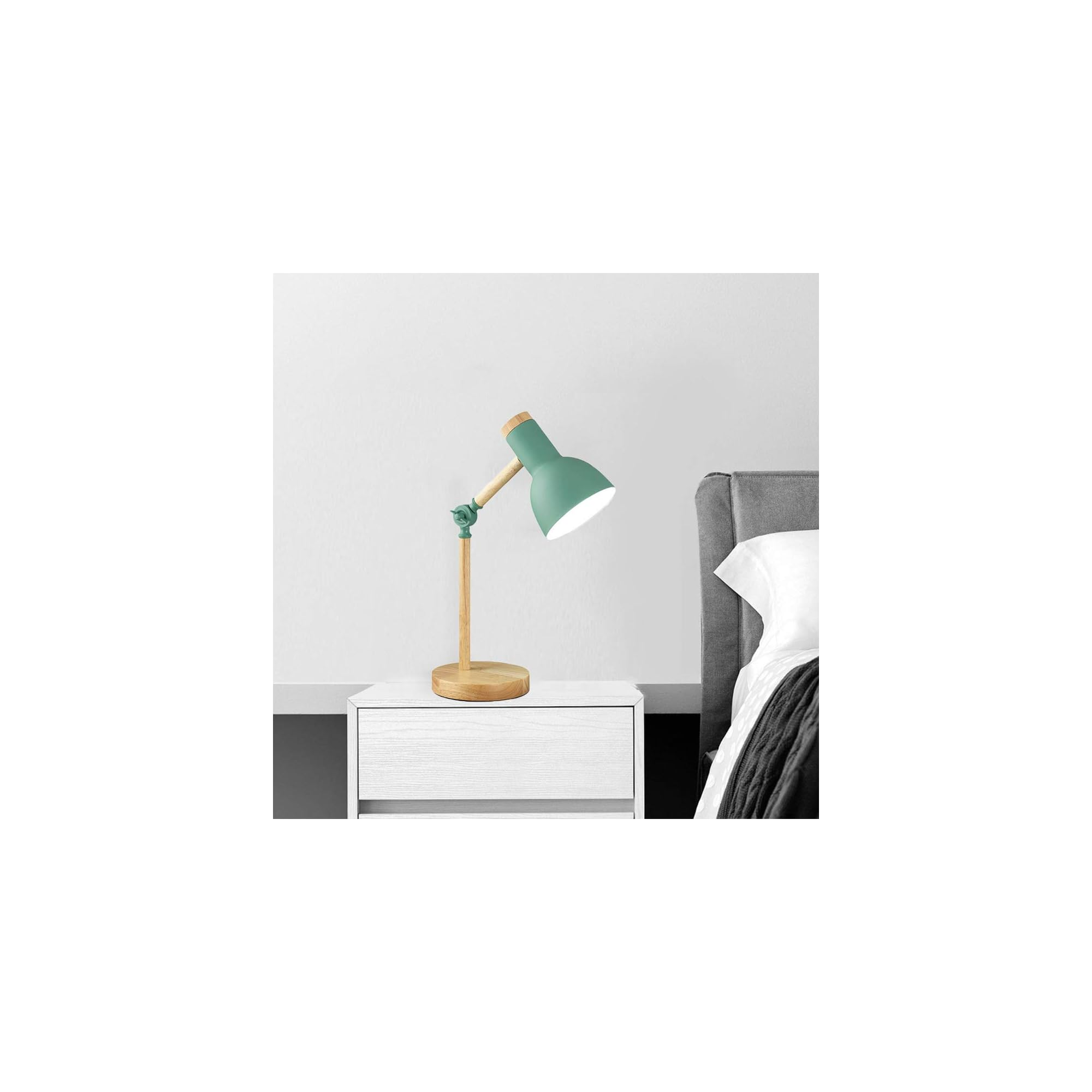 Grüne Schreibtischlampe mit Holzfuß auf weißem Nachttisch neben Bett.