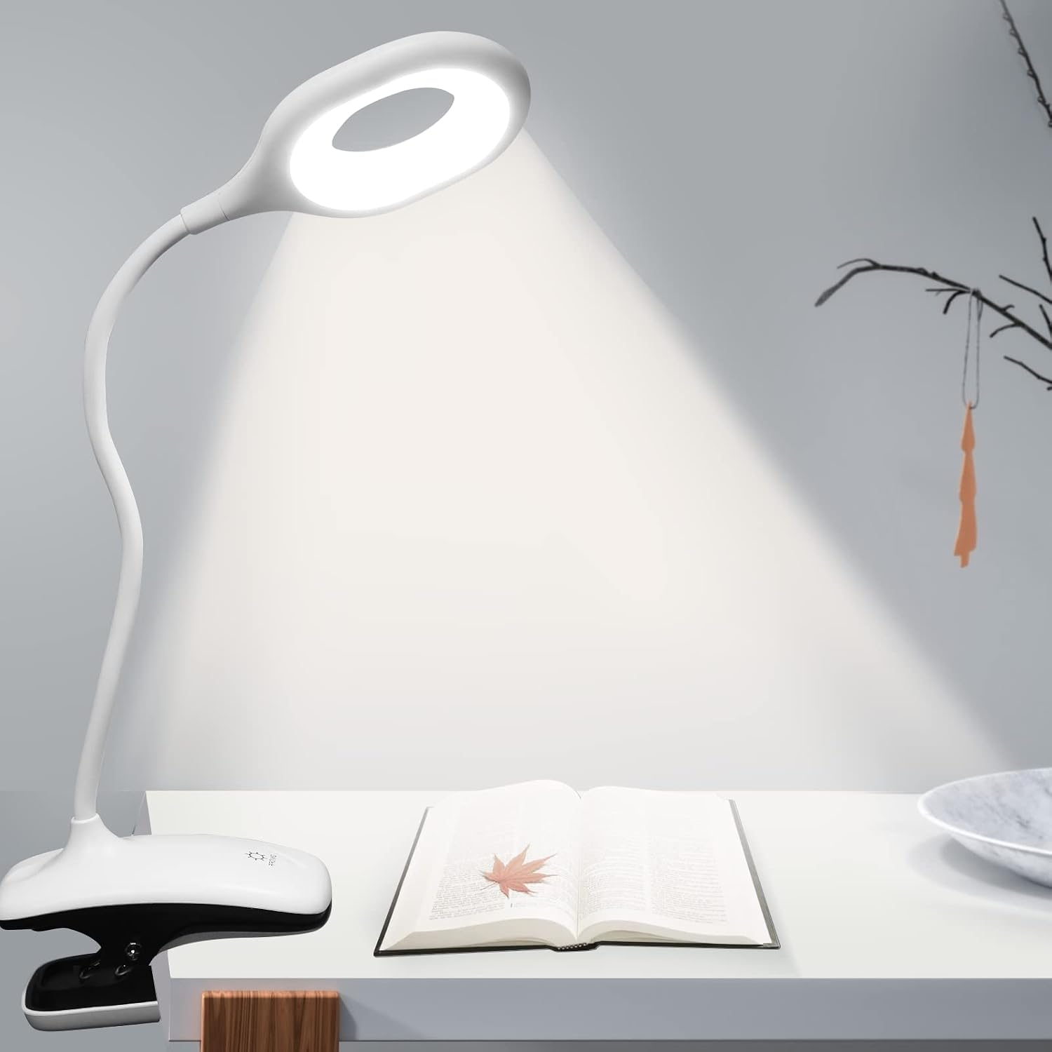 Eine weiße LED-Schreibtischlampe mit flexiblem Hals beleuchtet ein offenes Buch mit einem Blatt auf der Seite.