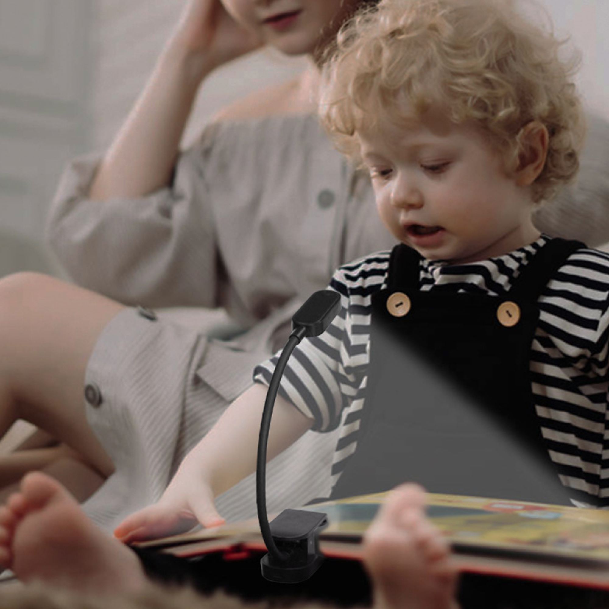 Ein Kind mit blonden Locken liest mit einer Frau ein Buch, beleuchtet von einer Klemmlampe.