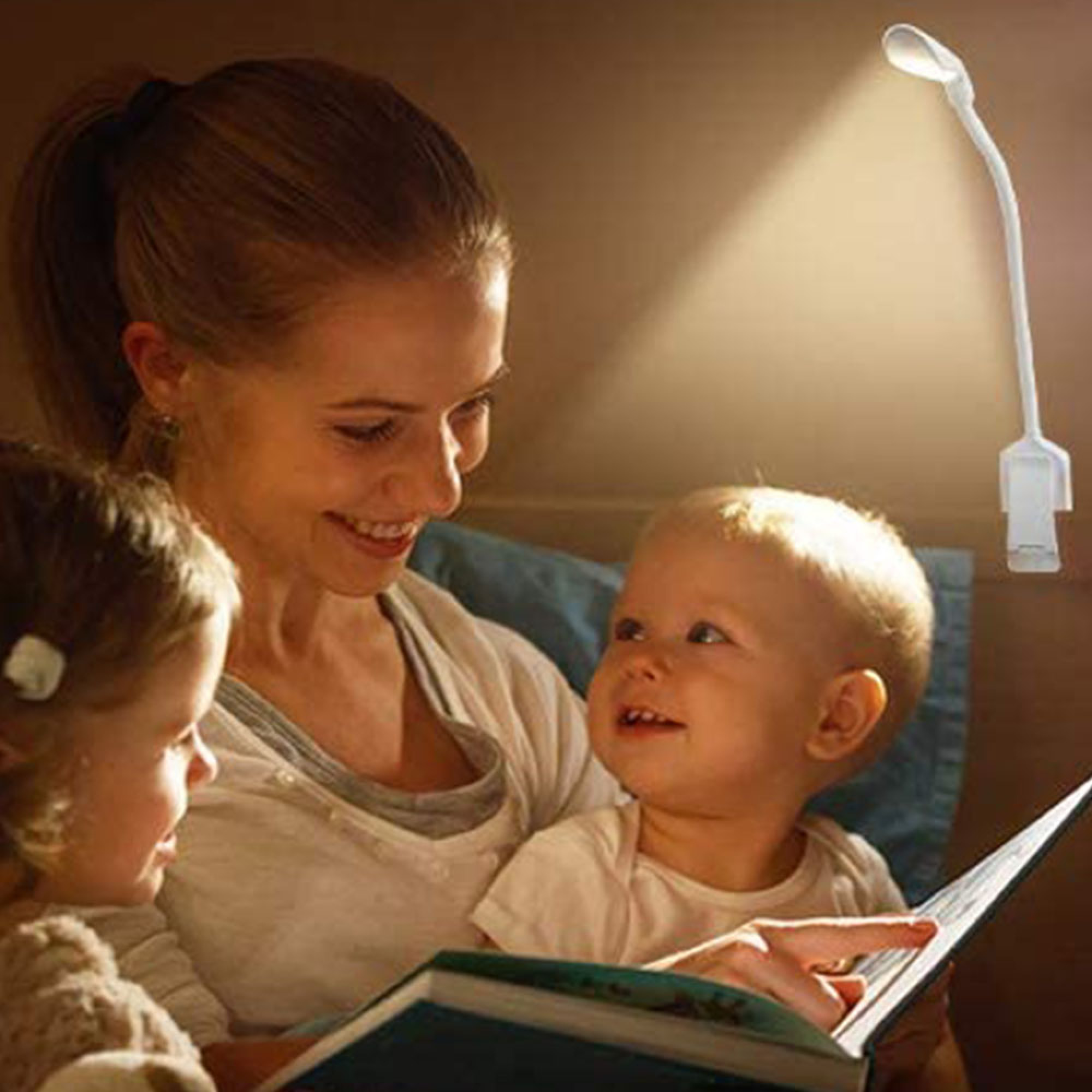 Eine Frau liest zwei Kindern unter einer Klemmlampe vor. Warmes Licht beleuchtet sie.