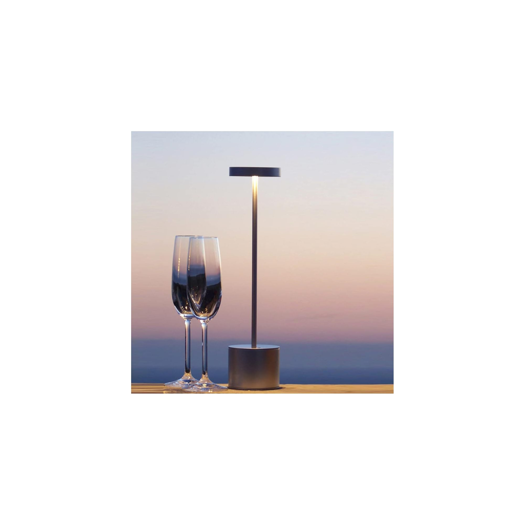 Zwei Weingläser und eine silberne Lampe auf einem Holztisch bei Sonnenuntergang.