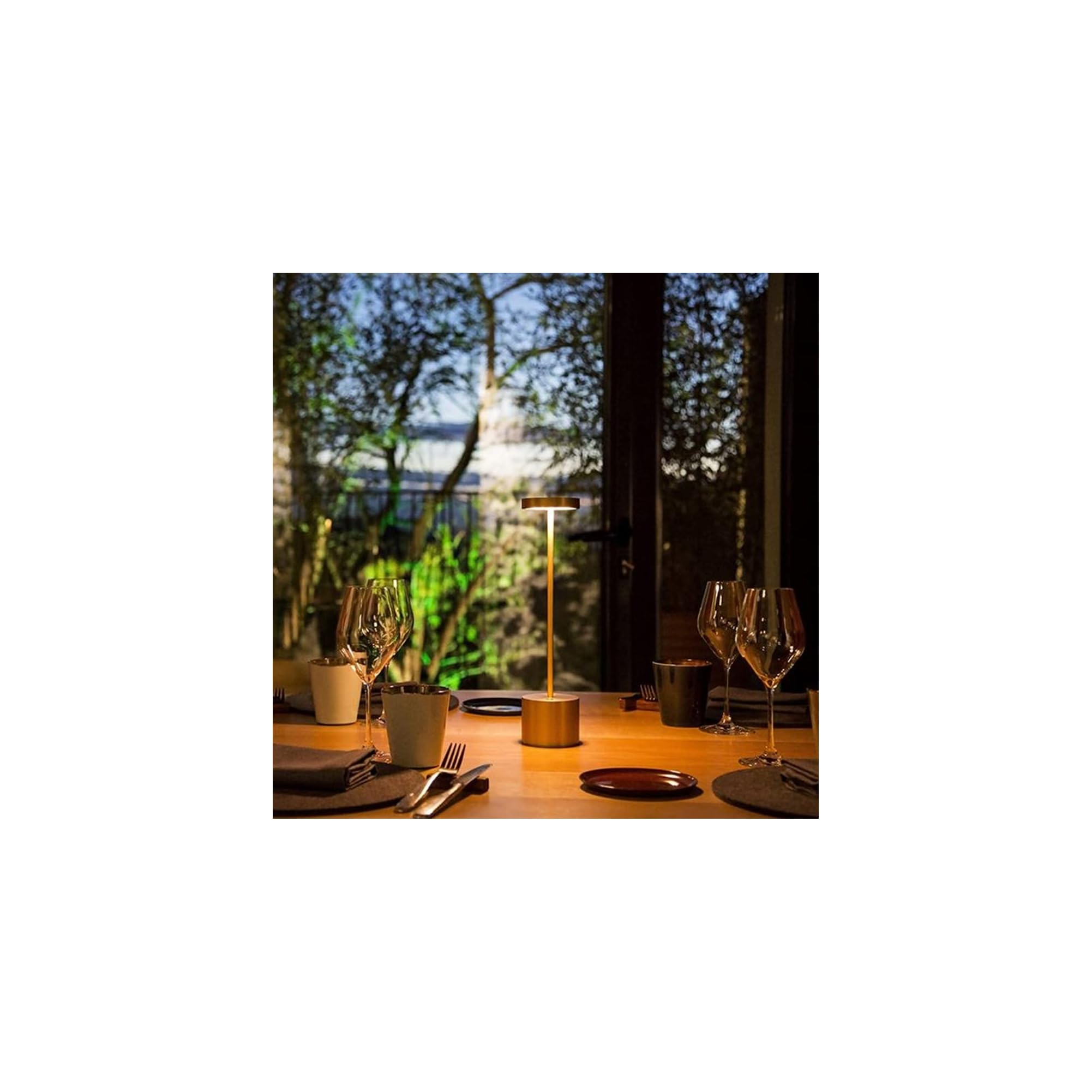 Ein goldener Tisch mit Gläsern, Besteck und einer Lampe. Draußen Bäume.