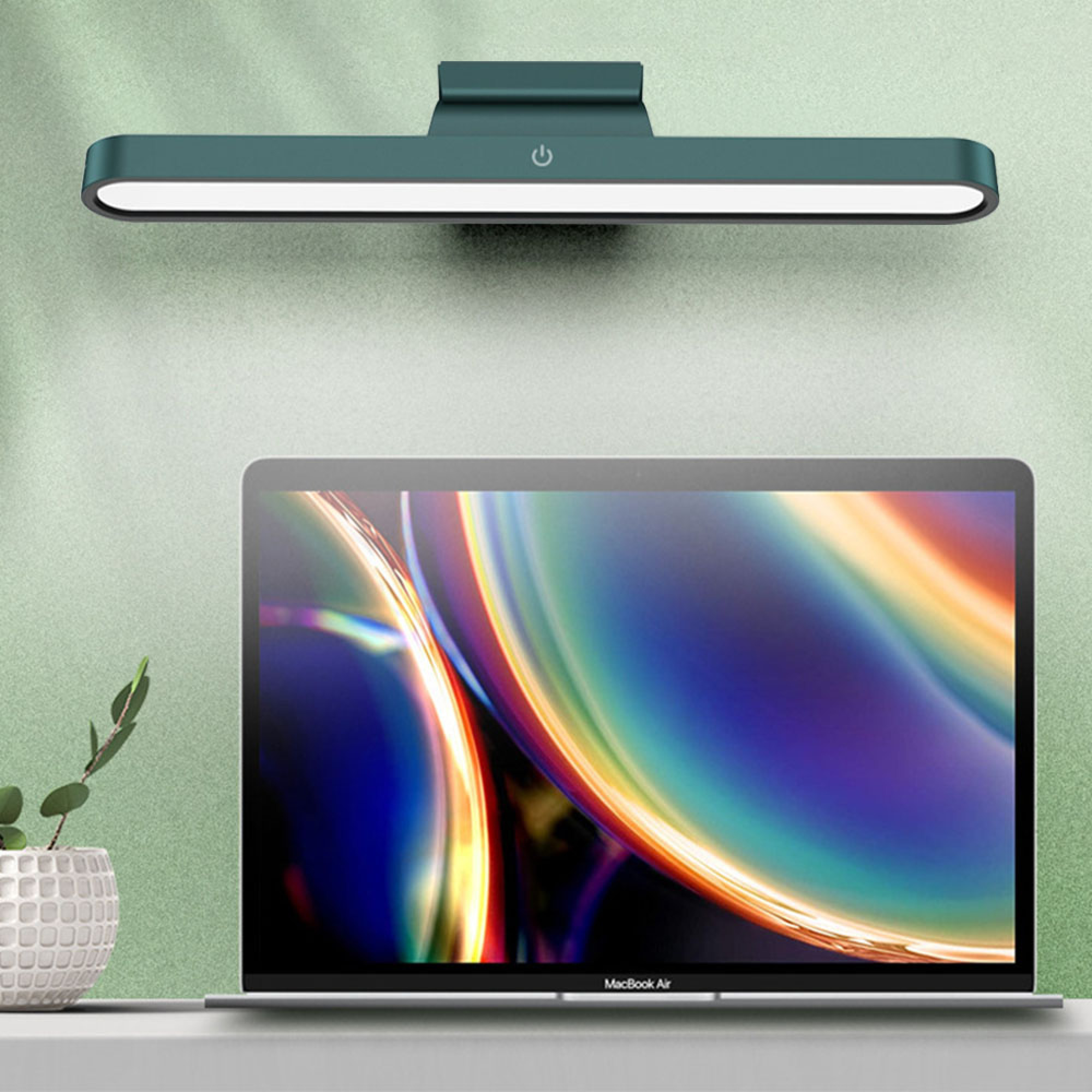 Eine grüne Schreibtischlampe über einem Laptop mit buntem Bildschirm.