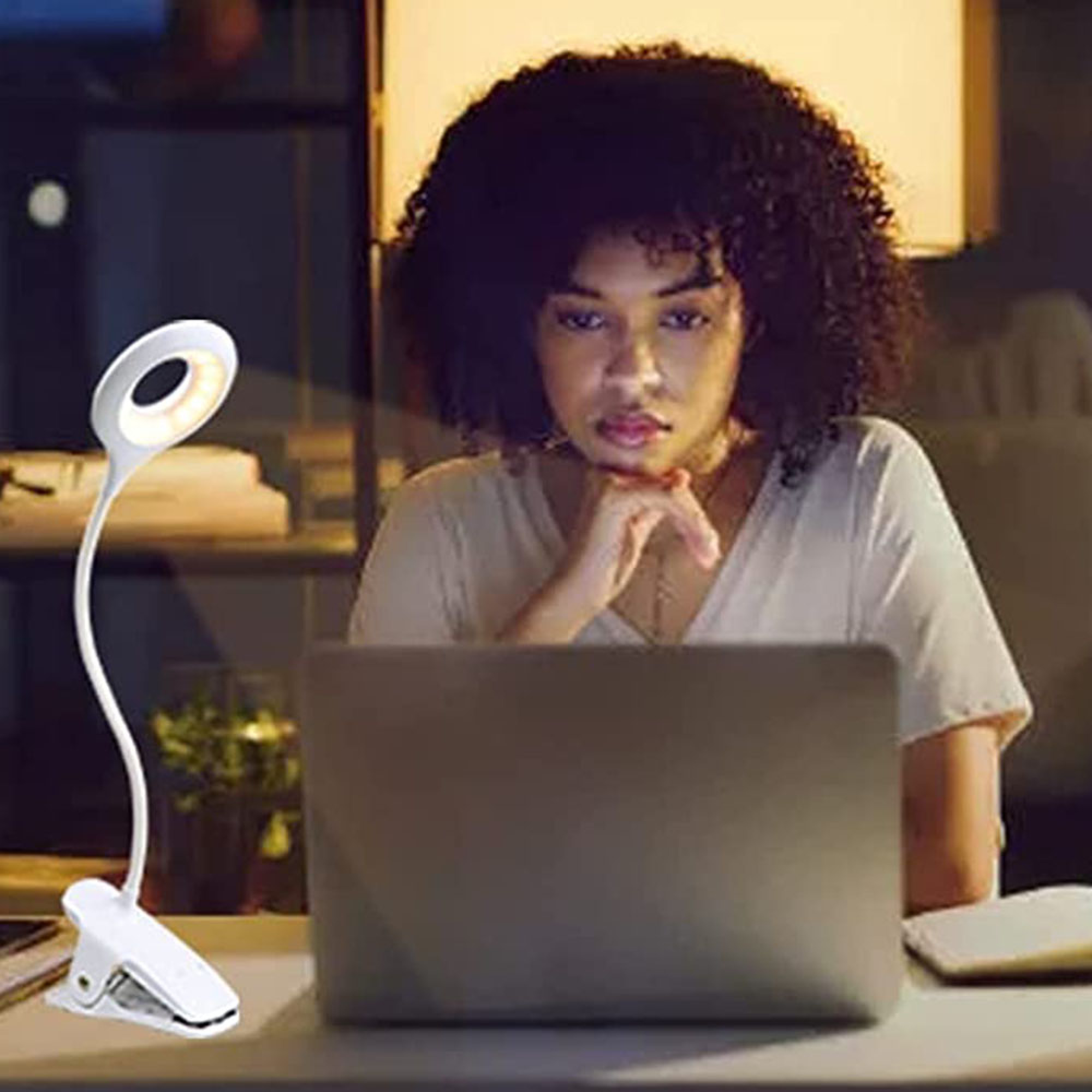 Eine Frau mit lockigem Haar sitzt am Laptop, beleuchtet von einer Klemmleuchte.