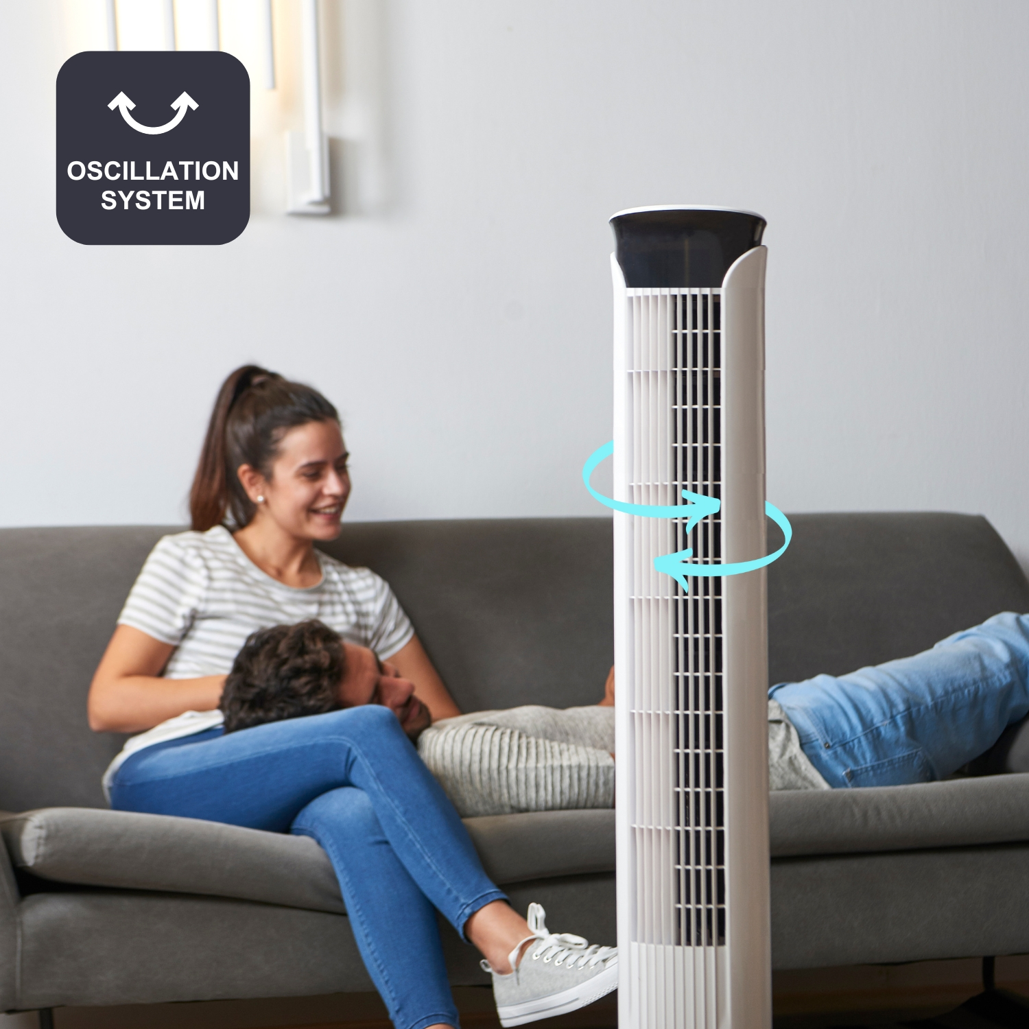 Un hombre apoya la cabeza en el regazo de una mujer sentada en un sofá. Un ventilador de torre está al lado.