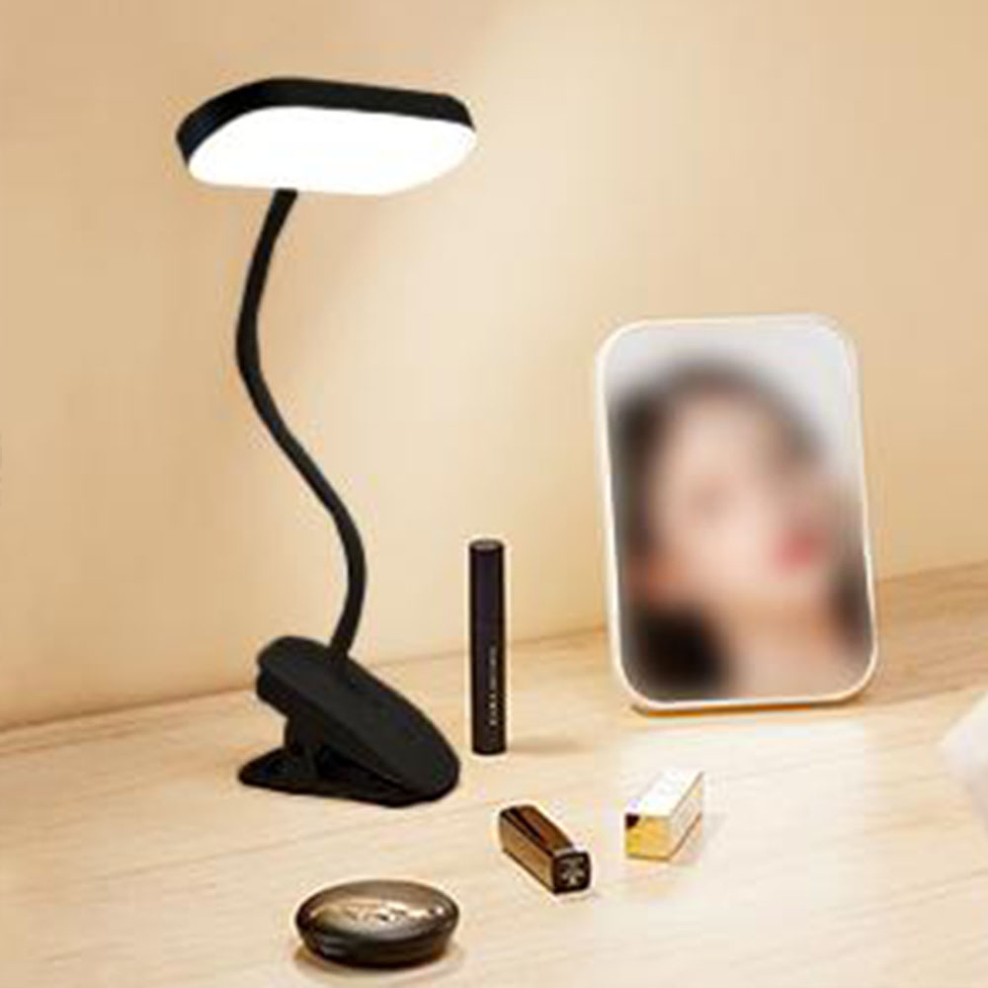 Ein schwarzes Klemmlicht leuchtet, daneben Lippenstift und ein Spiegel mit Frauengesicht.