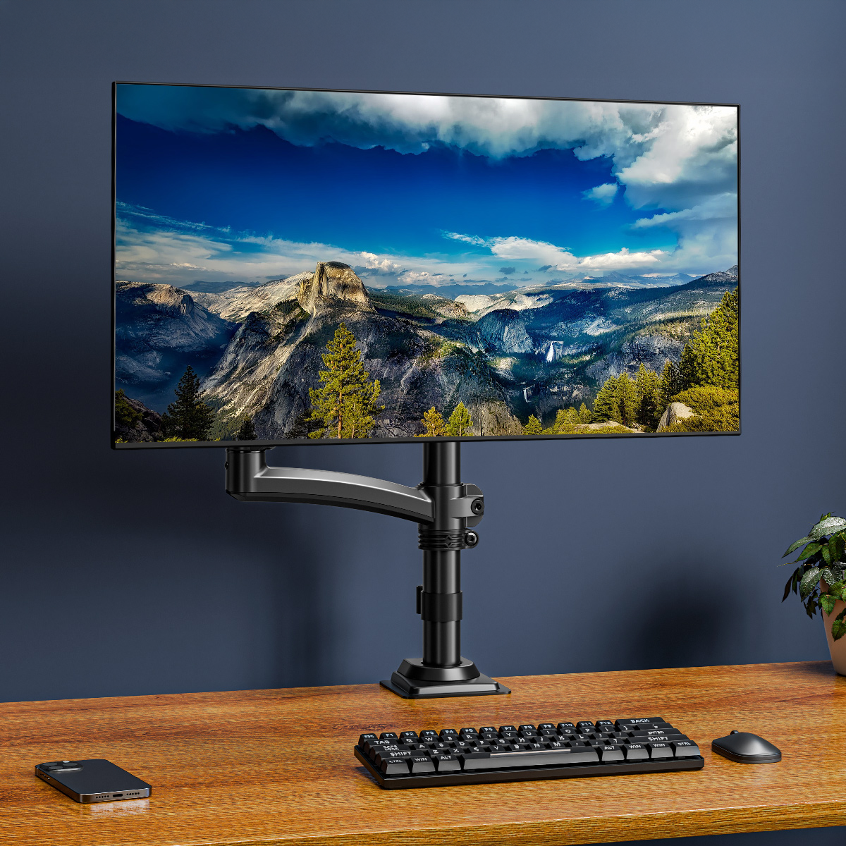 Monitor na regulowanym ramieniu stoi na biurku z klawiaturą, myszą i telefonem.