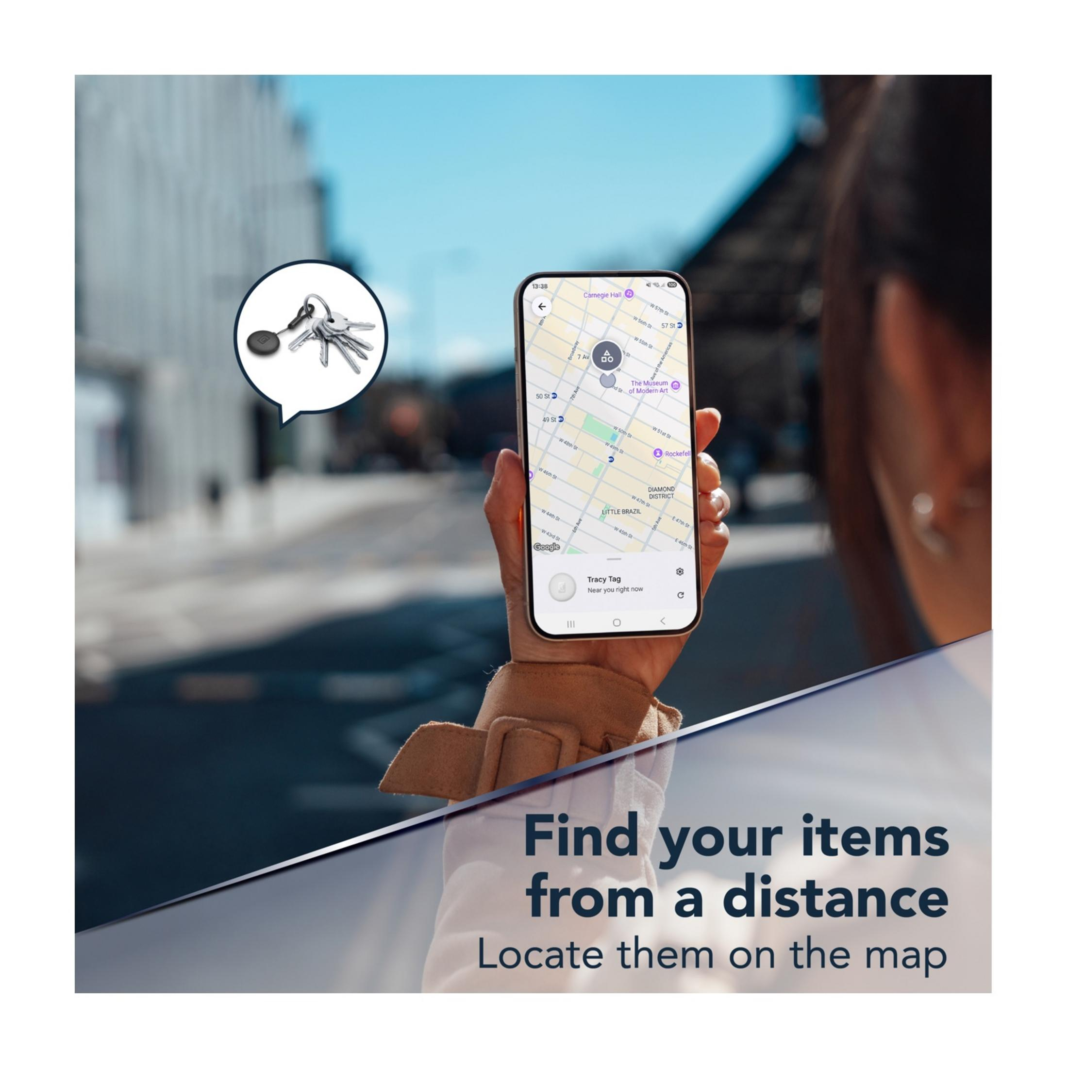 Schlüsselbund mit Tracker und Handy mit Karte. Im Hintergrund unscharfe Gebäude.