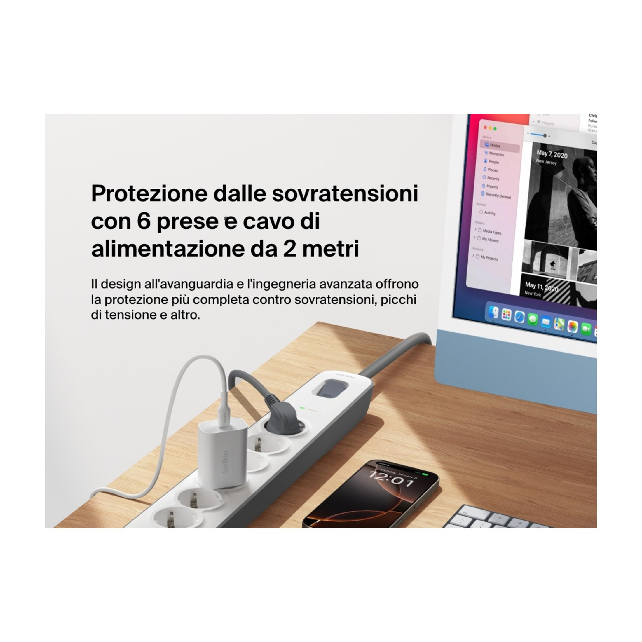 Multipresa bianca con dispositivi collegati e smartphone su scrivania in legno.