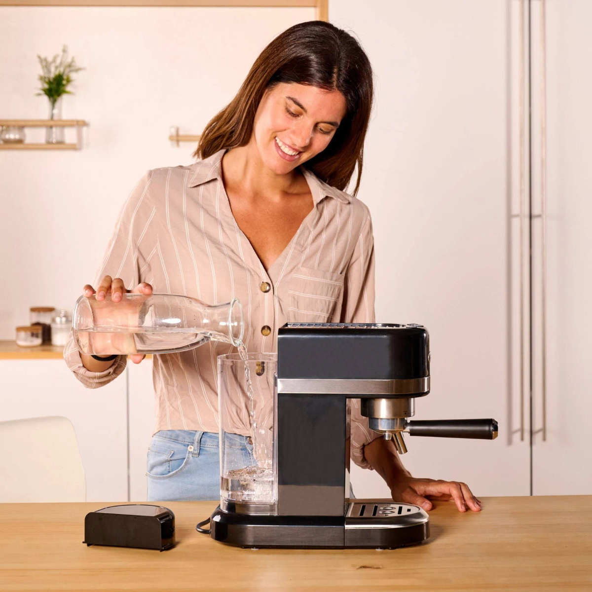 Una mujer vierte agua de una jarra en un vaso junto a una cafetera.