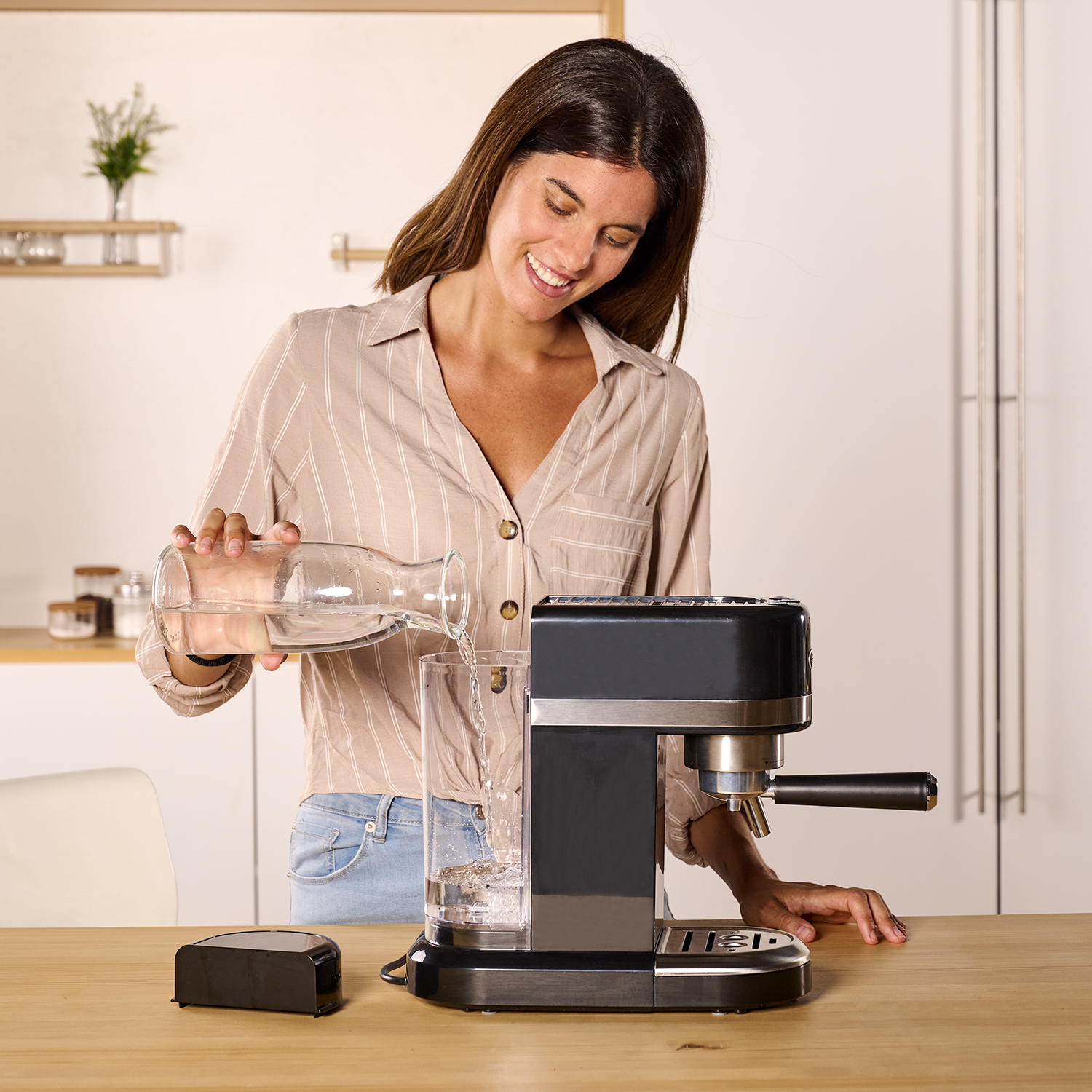 Una mujer vierte agua de una jarra en un vaso junto a una cafetera.