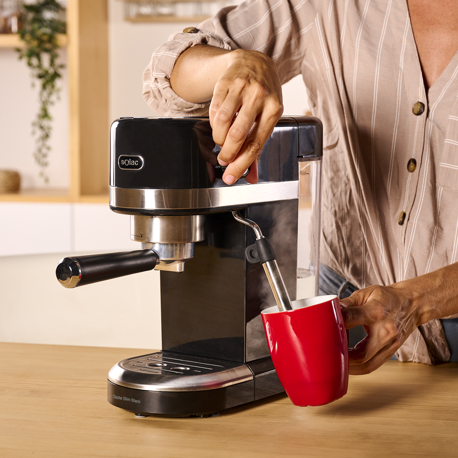 Una persona prepara café con una cafetera espresso negra, sosteniendo una taza roja.